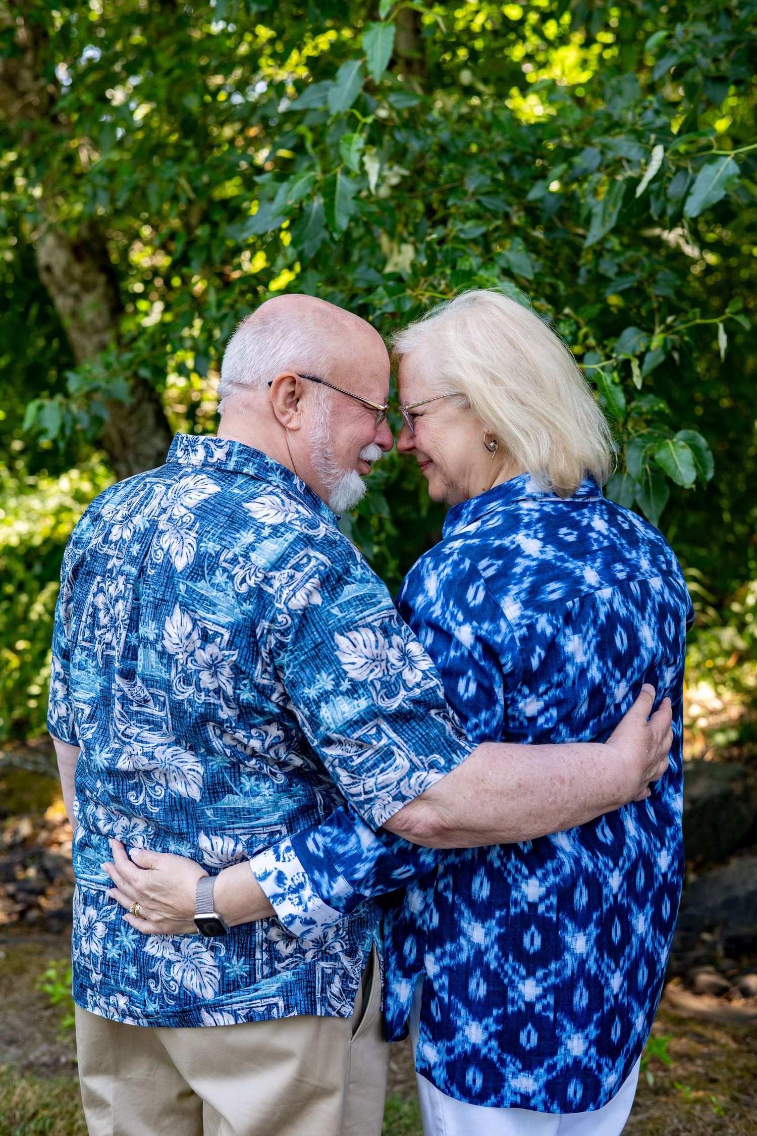 A couple in matching blue and white patterned outfits embracing outdoors against a green leafy backdrop.