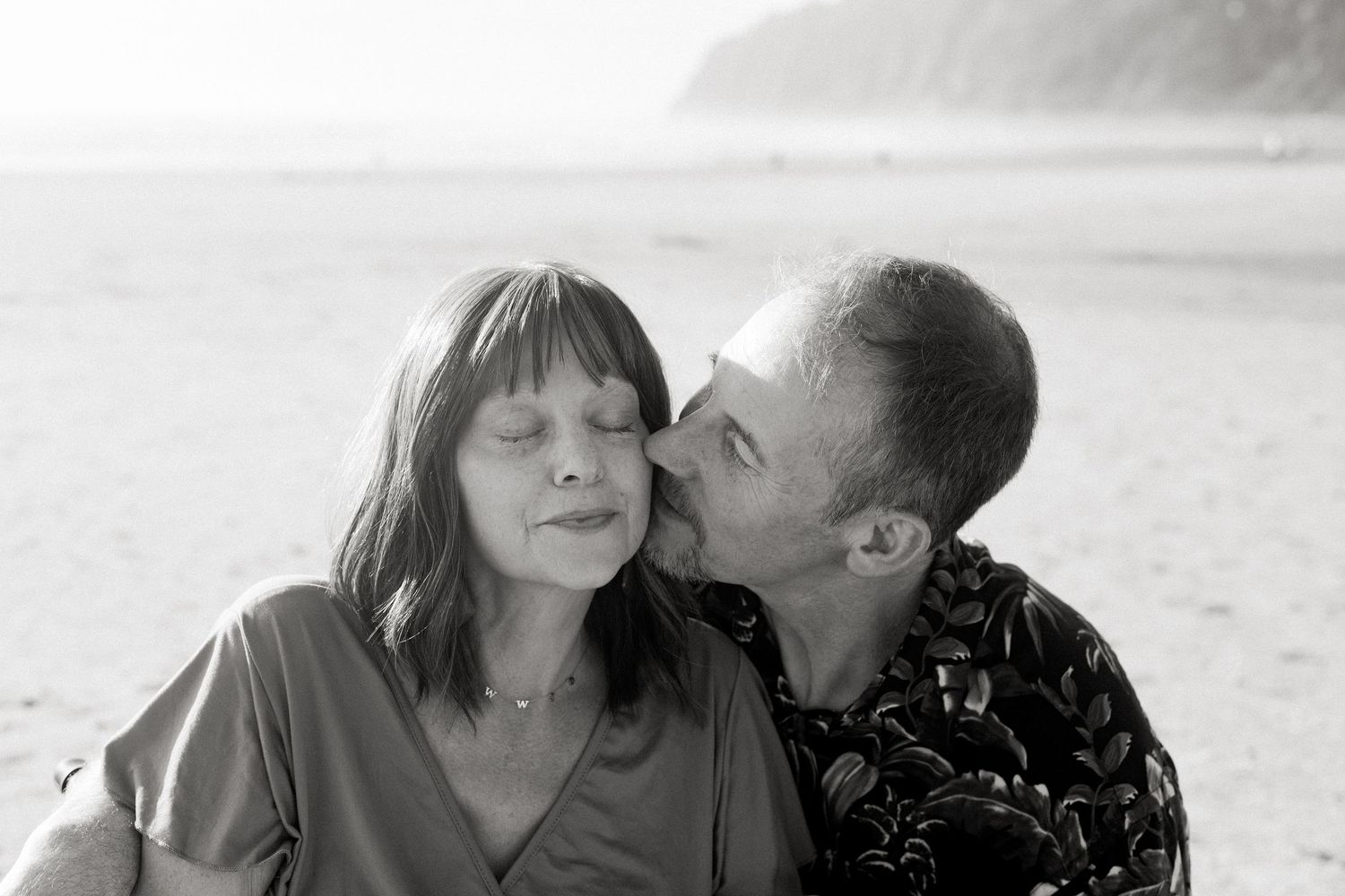 Black and white romantic photos show a couple sharing intimate moments on a beach in four connected images.