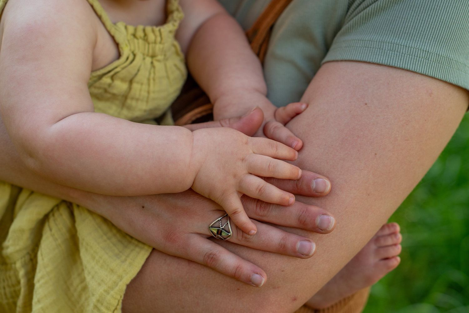 A child's small hand rests gently on an adult's arm while wearing a yellow dress.