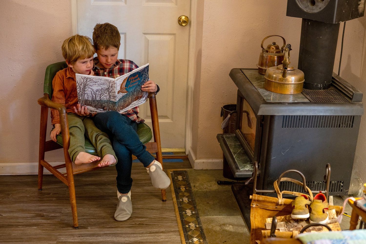 Two young friends sit together on a wooden floor reading a magazine and sharing a relaxing moment together.