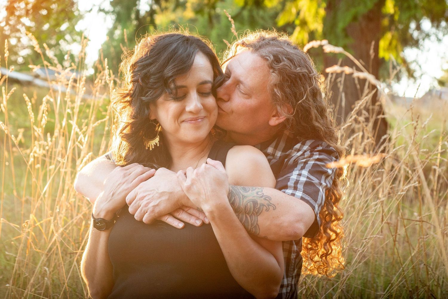 Couple embraces in golden sunlit field during summer sunset engagement photoshoot session.