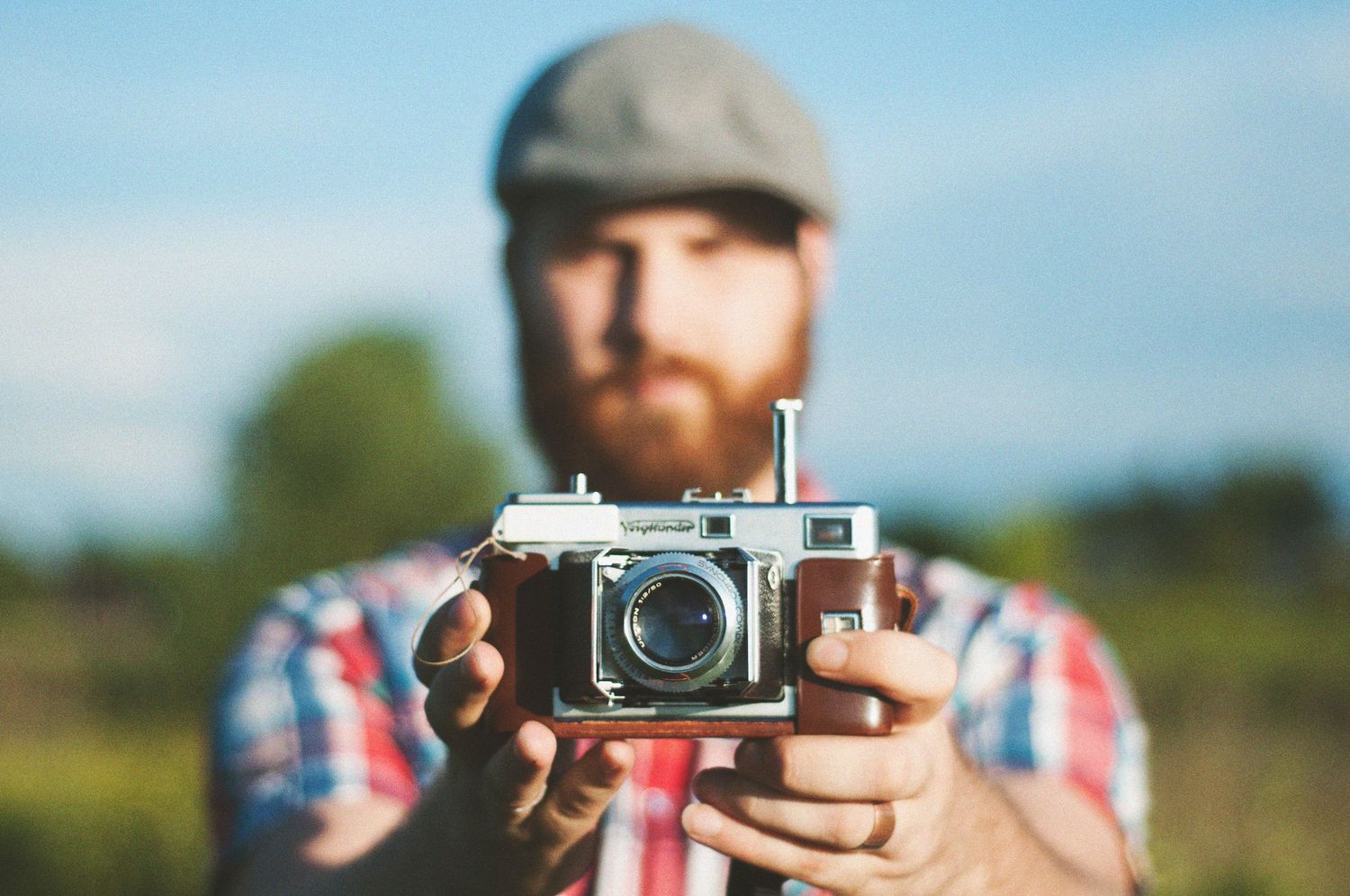 Close-up of vintage camera being held against blurred outdoor background.