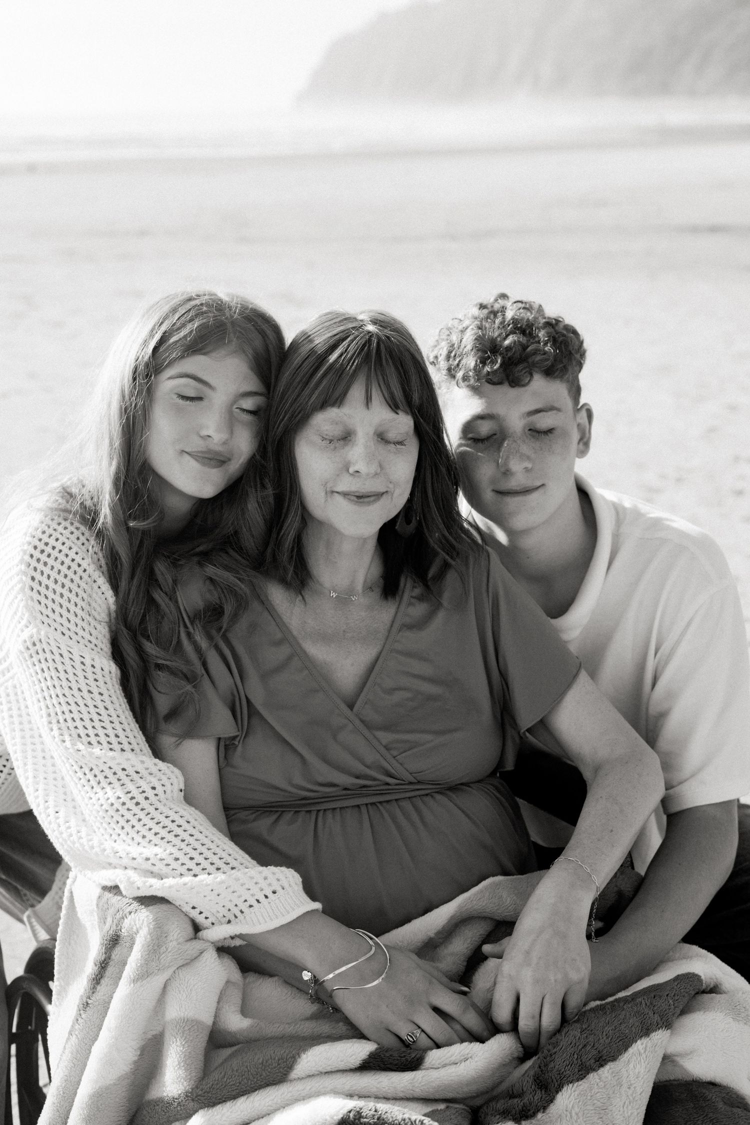Three individuals share a tender black and white moment while embracing on a couch.