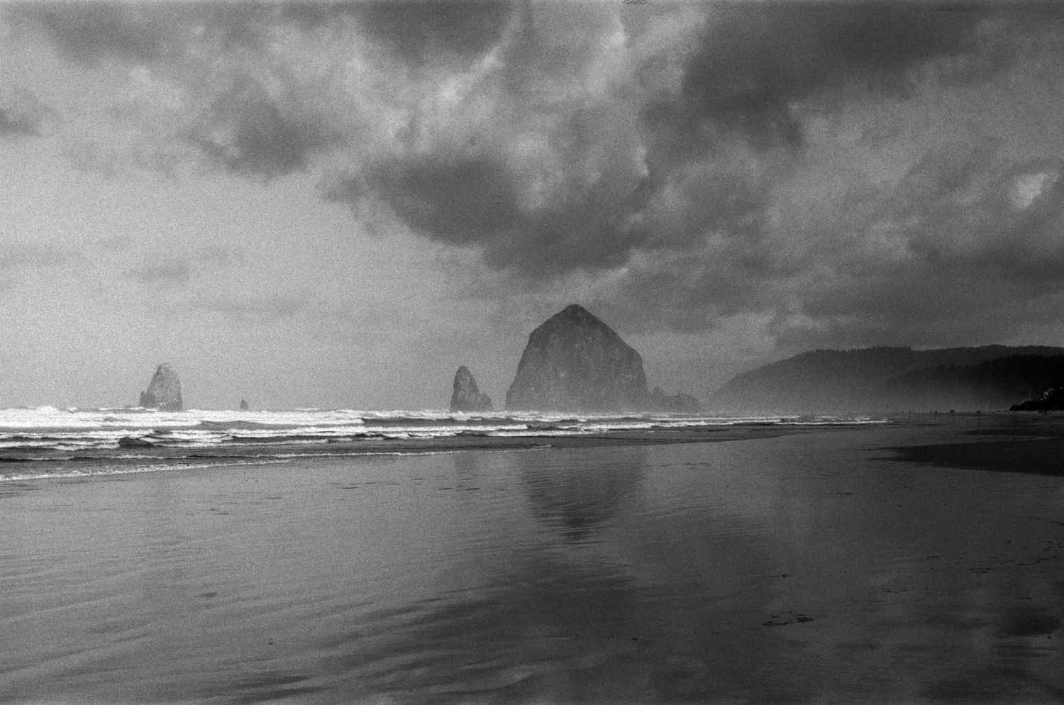 Dramatic black and white coastal landscape with stormy clouds over ocean waves and rocky cliffs.