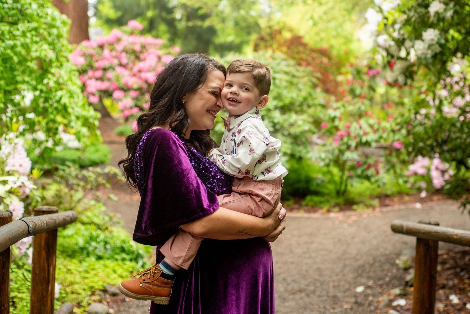 A loving moment shared outdoors in a lush garden path with blooming pink azaleas in the background.
