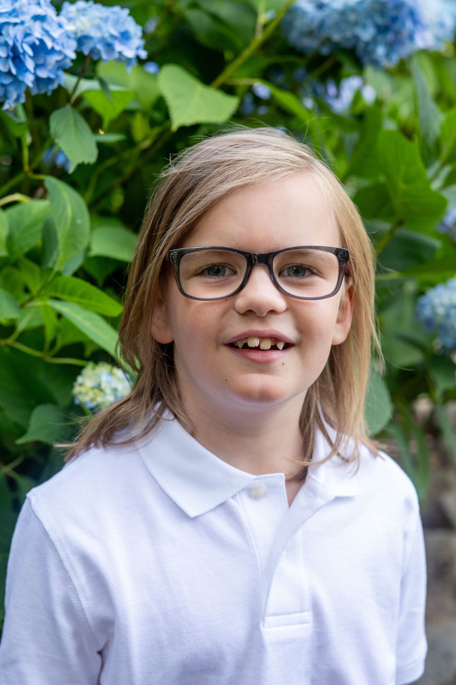 A sequence of four close-up photos showing a smiling child in a white polo shirt and glasses outdoors with greenery in background.