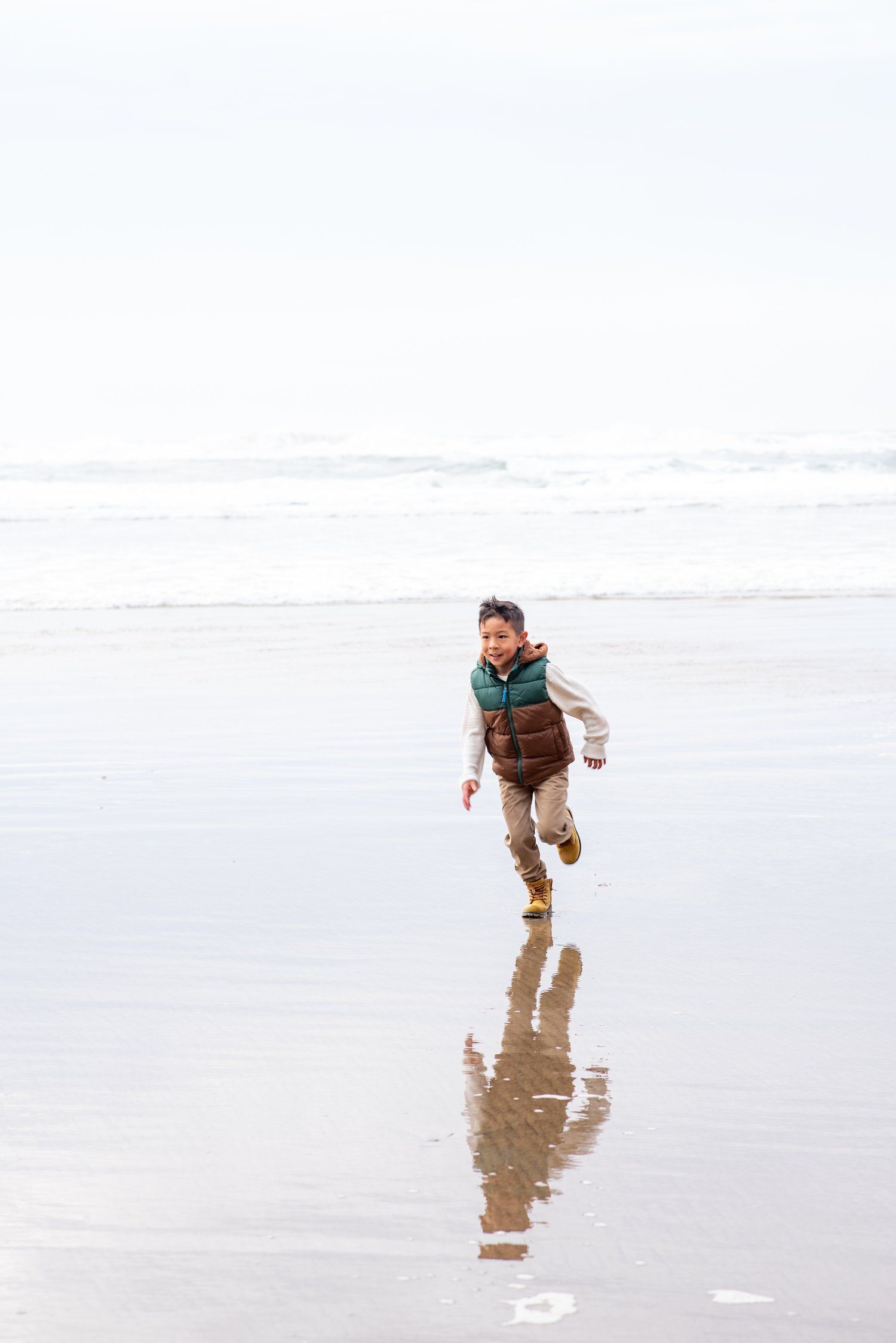 Person running and playing on wet sandy beach at low tide.