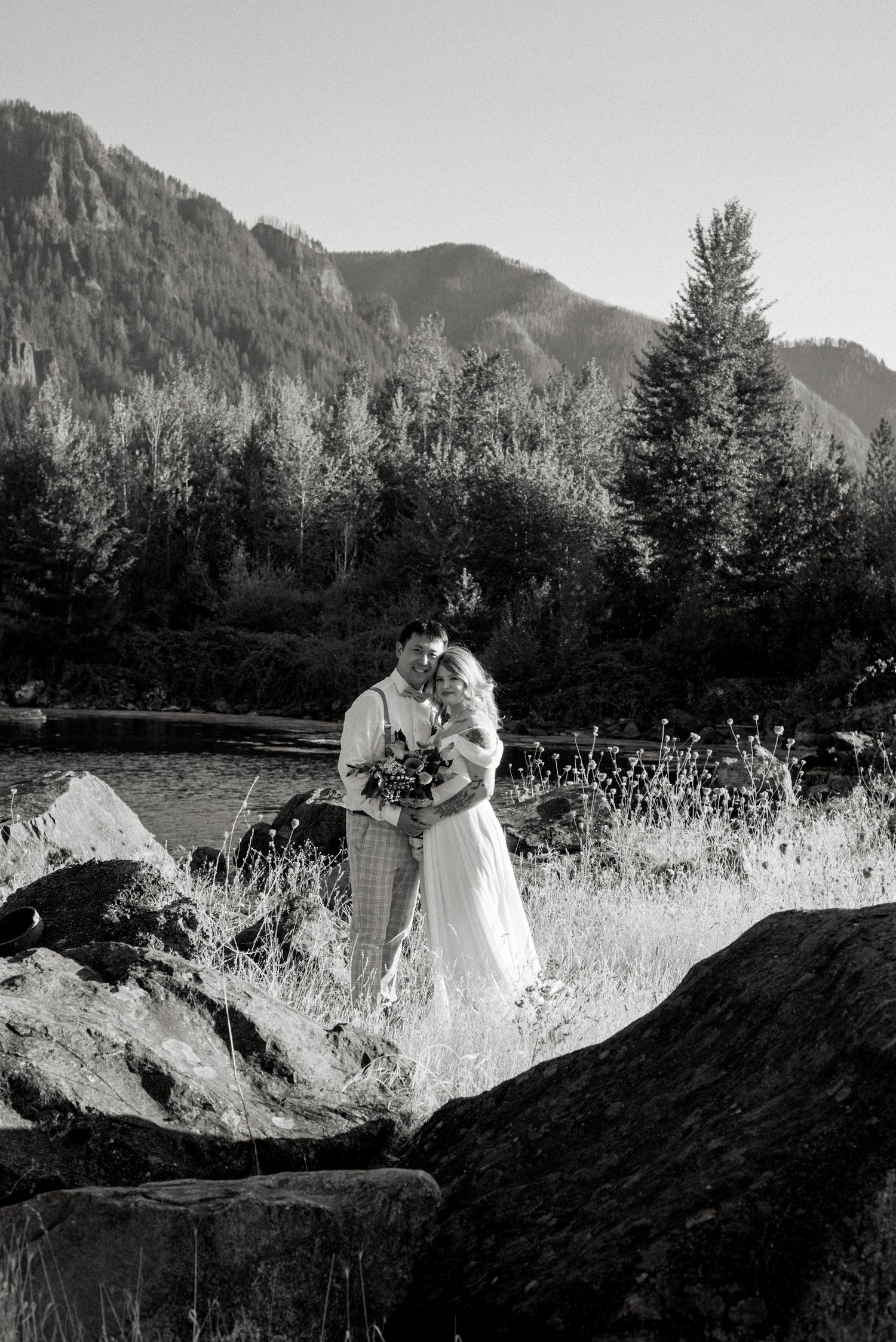 A black and white wedding portrait with mountain scenery and evergreen trees in the background.
