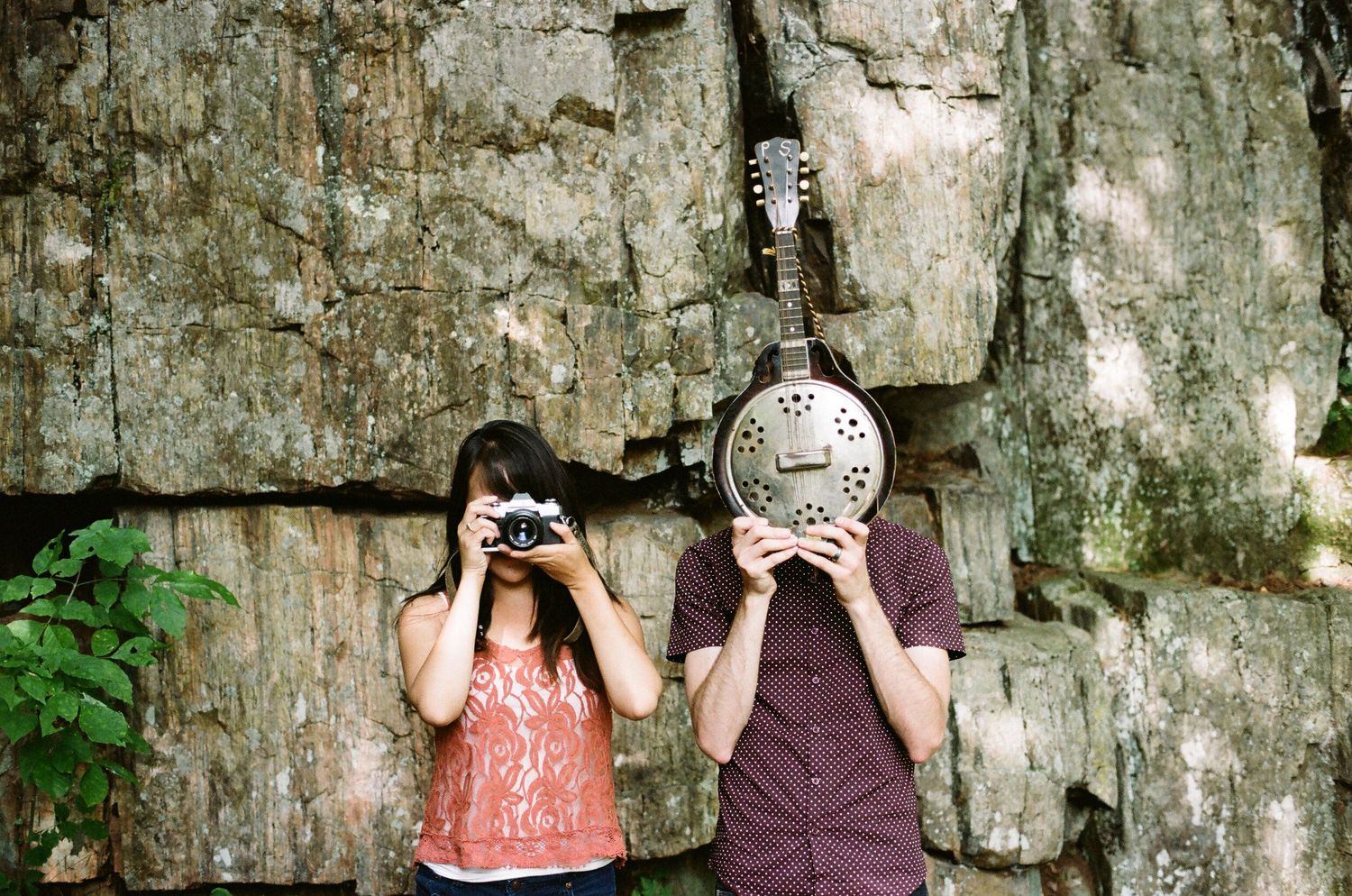 A series of people hold digital cameras against a stone wall backdrop to take photos at various angles.