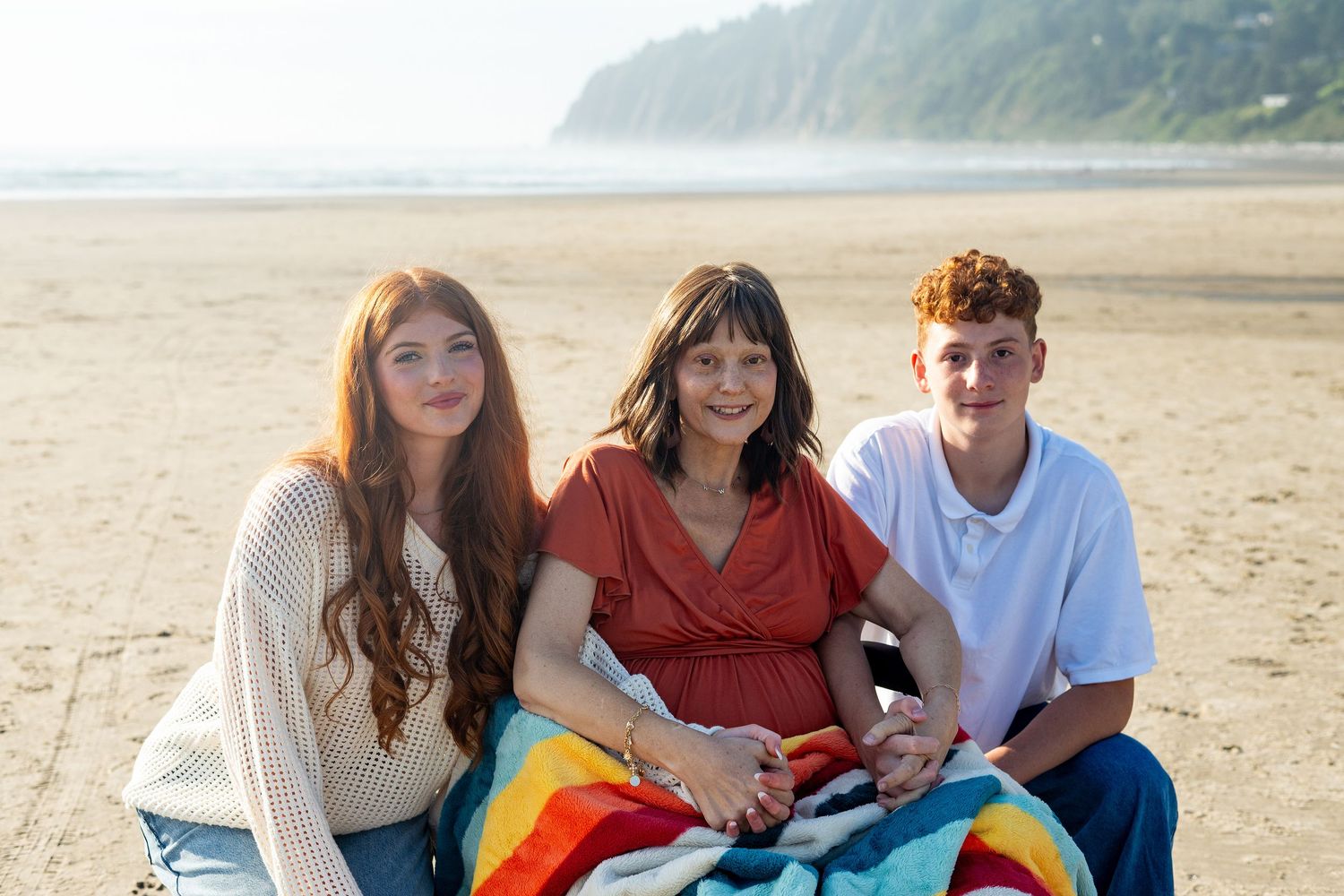 Four friends enjoy a relaxing day at the beach while sitting on colorful blankets and sharing conversation.