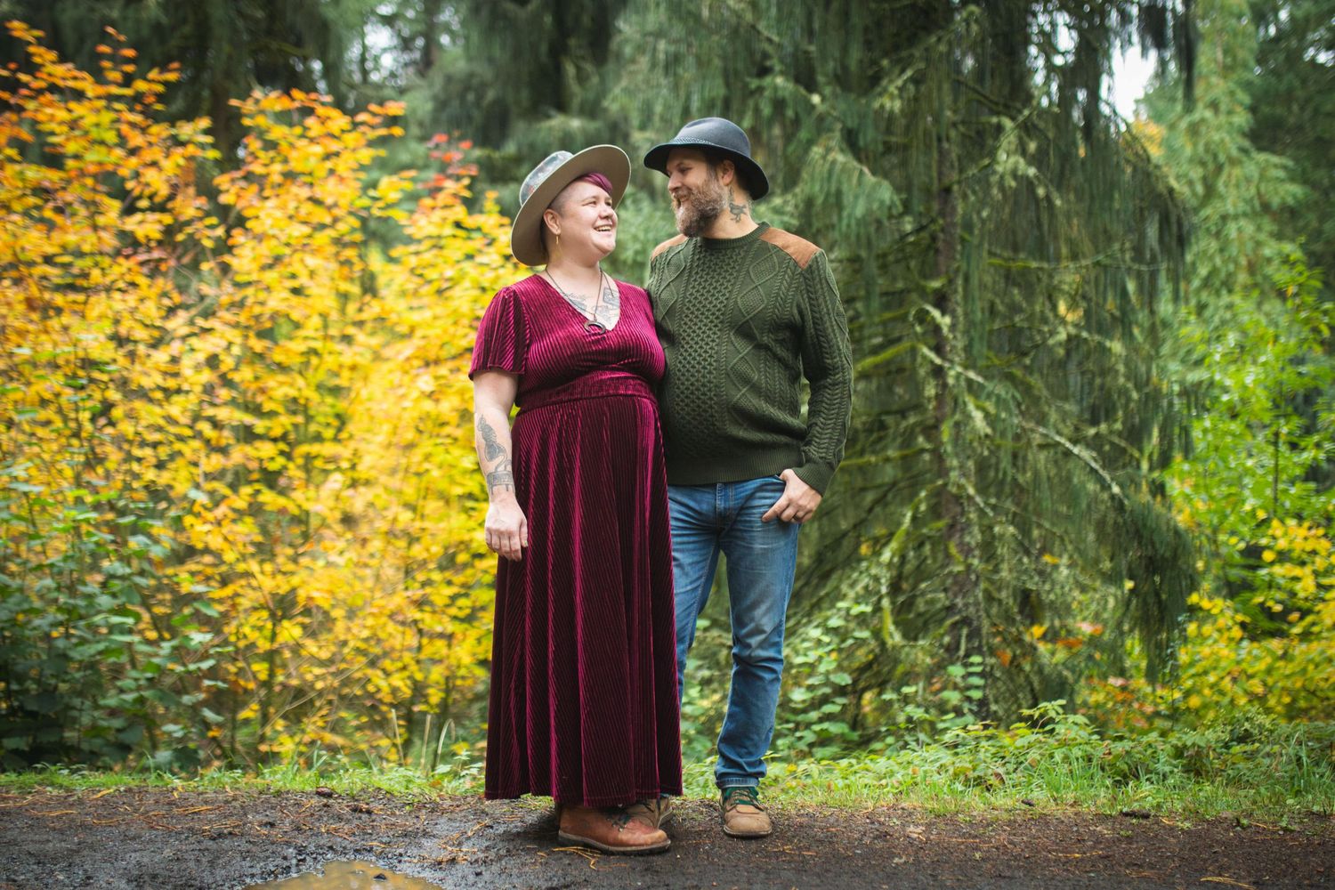 A couple shares a tender moment on a forest path with vibrant yellow autumn foliage in the background.