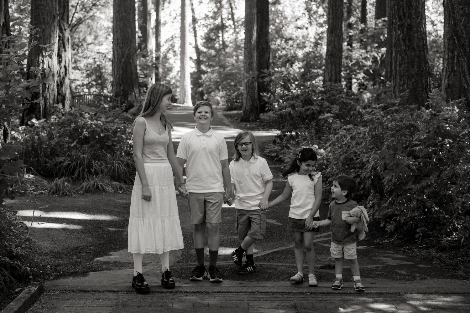A group stands together on a forest path surrounded by tall trees and lush greenery in black and white.