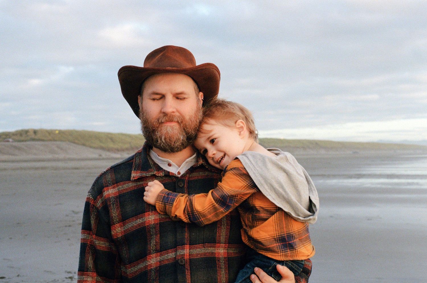 Two figures in plaid flannels embrace on cloudy beach.