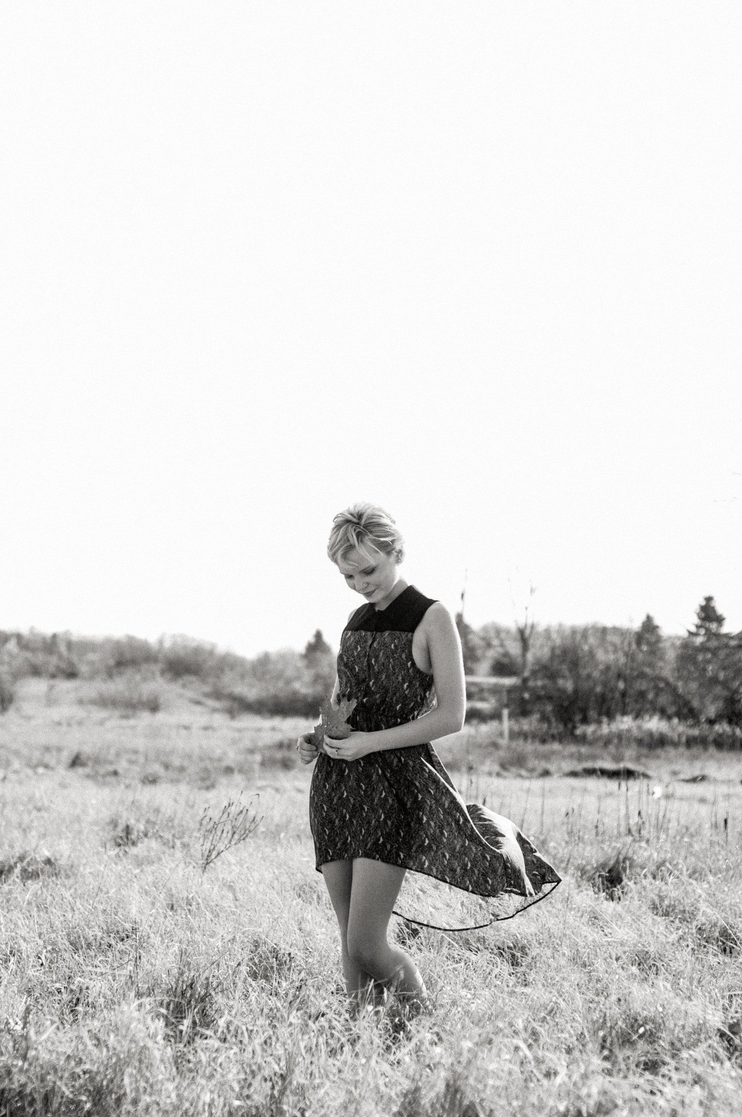 A black and white portrait of someone twirling in a dress in a sunny meadow.