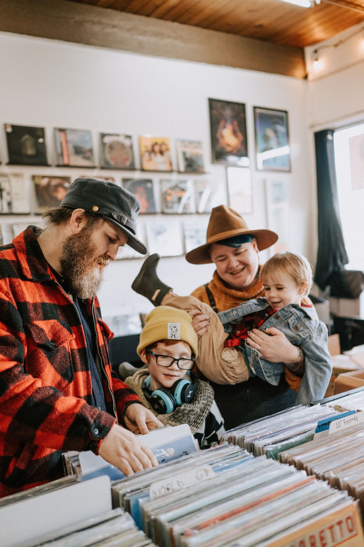 Family browses vinyl records together at a music store with mounted album covers on the wall behind them.