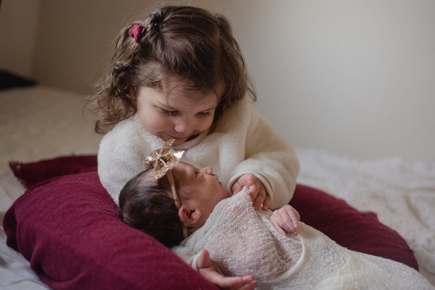 A tender moment between two siblings on a burgundy blanket.
