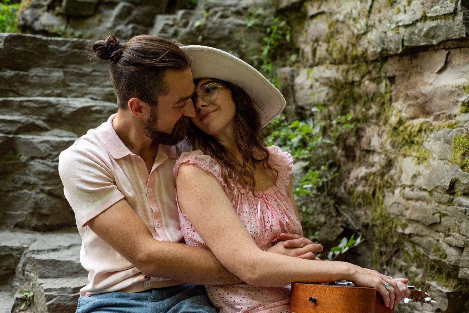 Romantic couple embracing near rustic stone wall during outdoor photo session.
