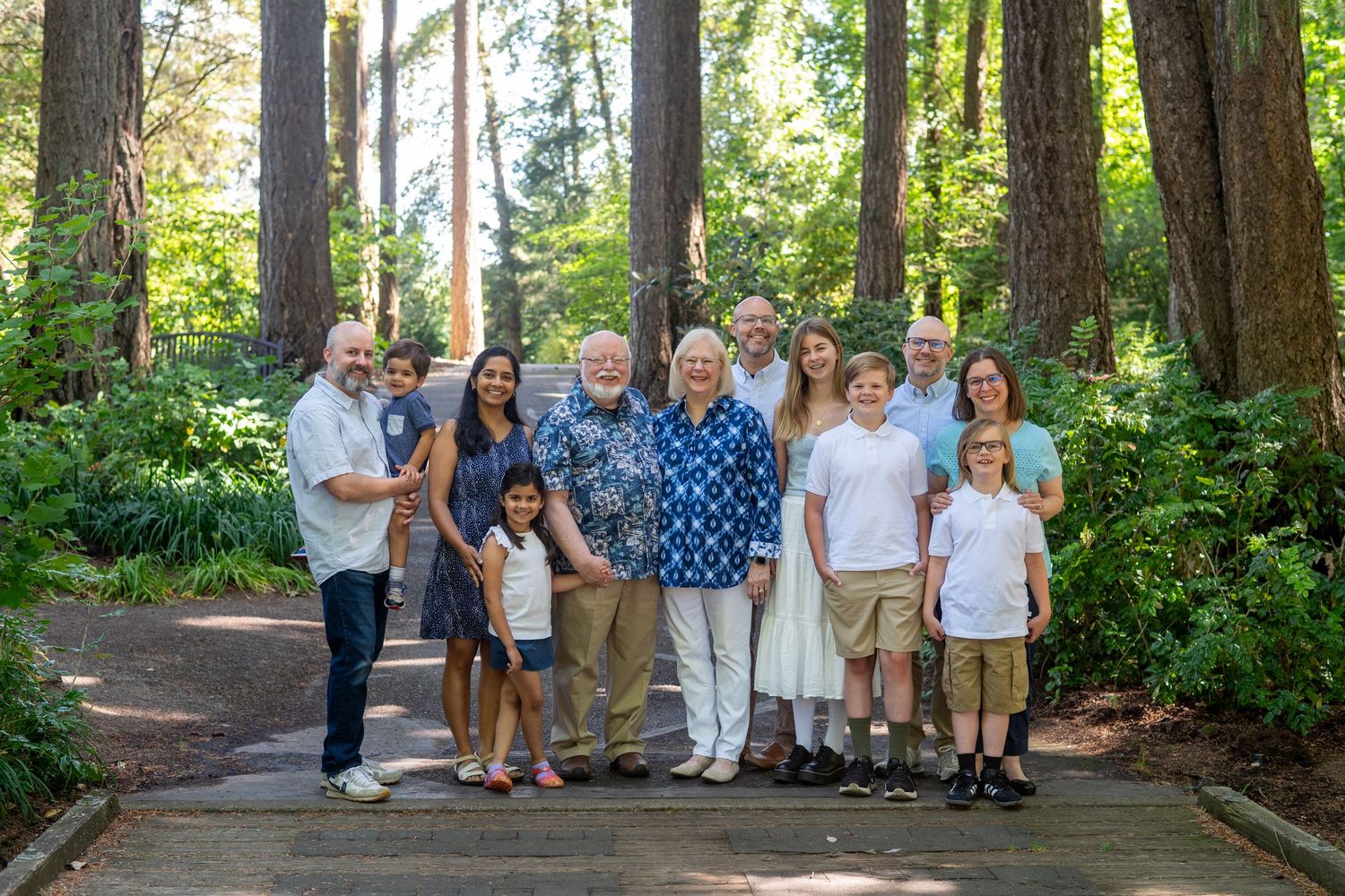 People gather outdoors for portraits in a lush green park setting surrounded by tall trees and natural foliage.