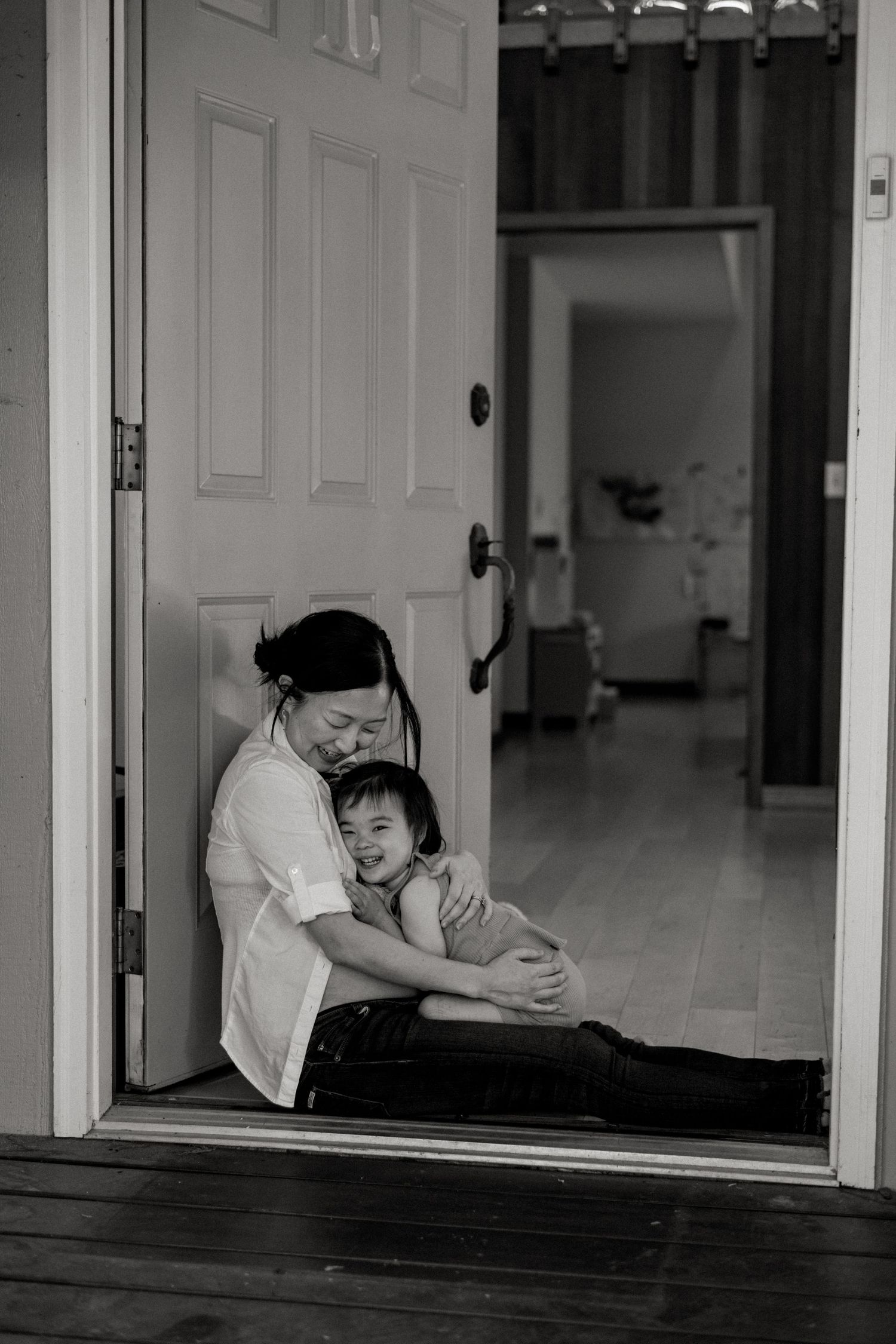 Tender embrace shared in doorway of modern home hallway in black and white.