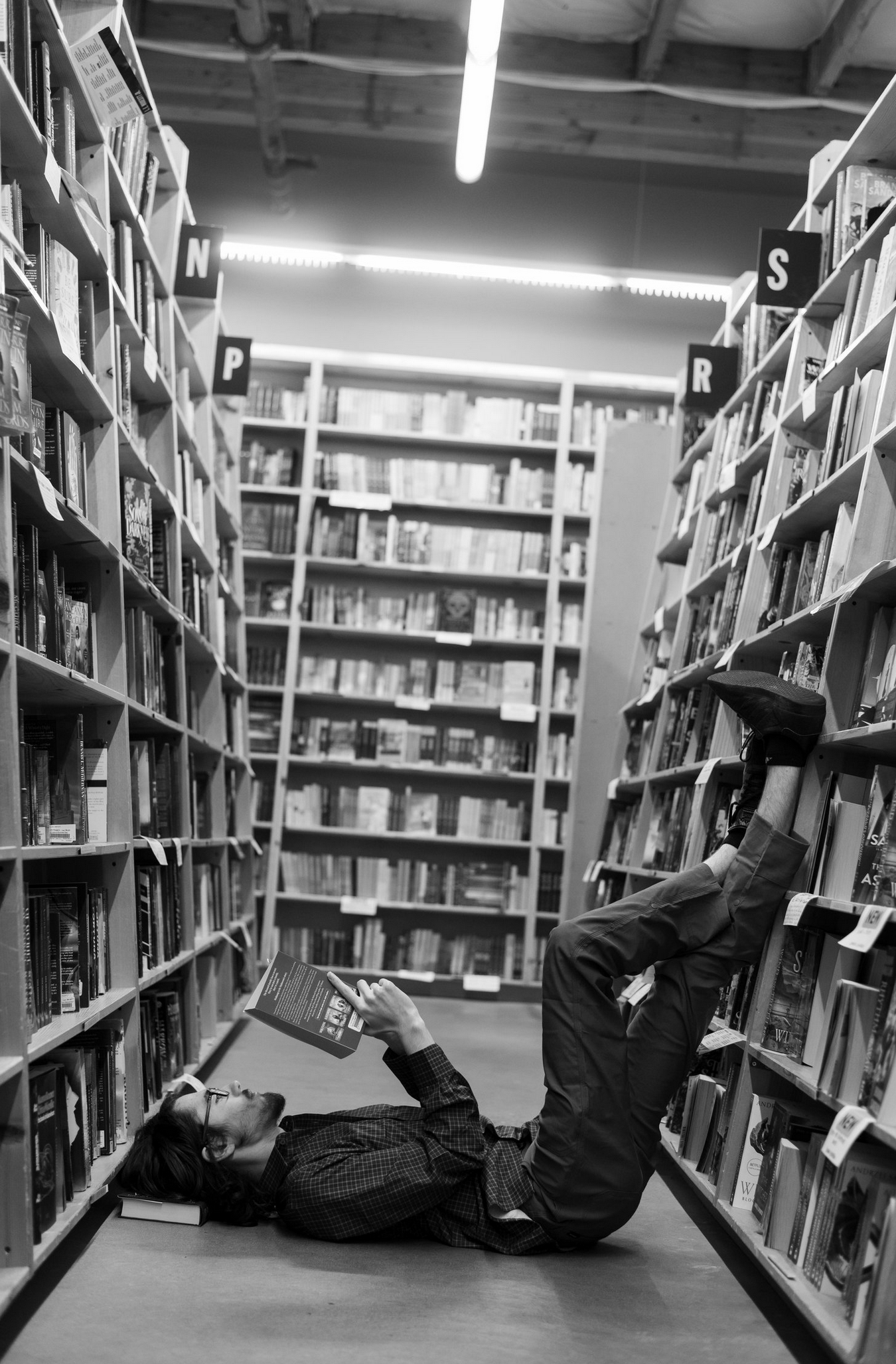 A black and white photo of someone lying dramatically between library bookshelves.