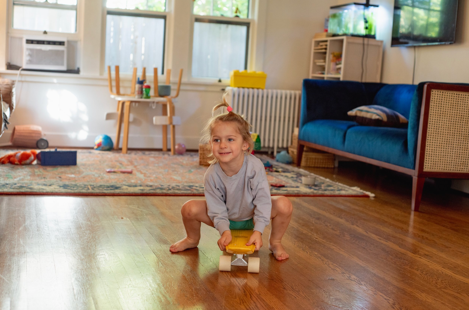 Small child plays with yellow toy car on wooden floor in playroom.