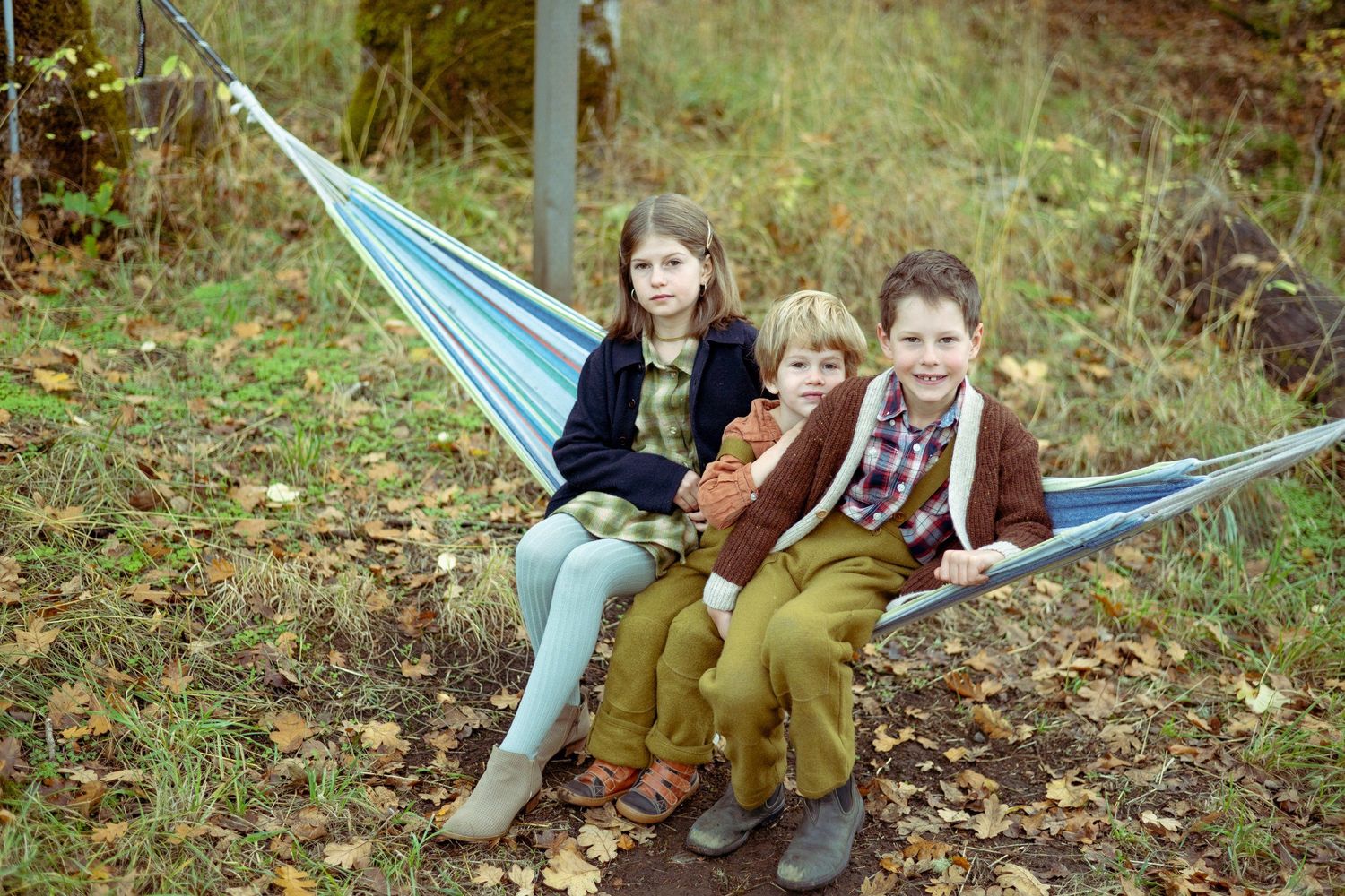Three children relaxing together in a blue hammock during fall season.