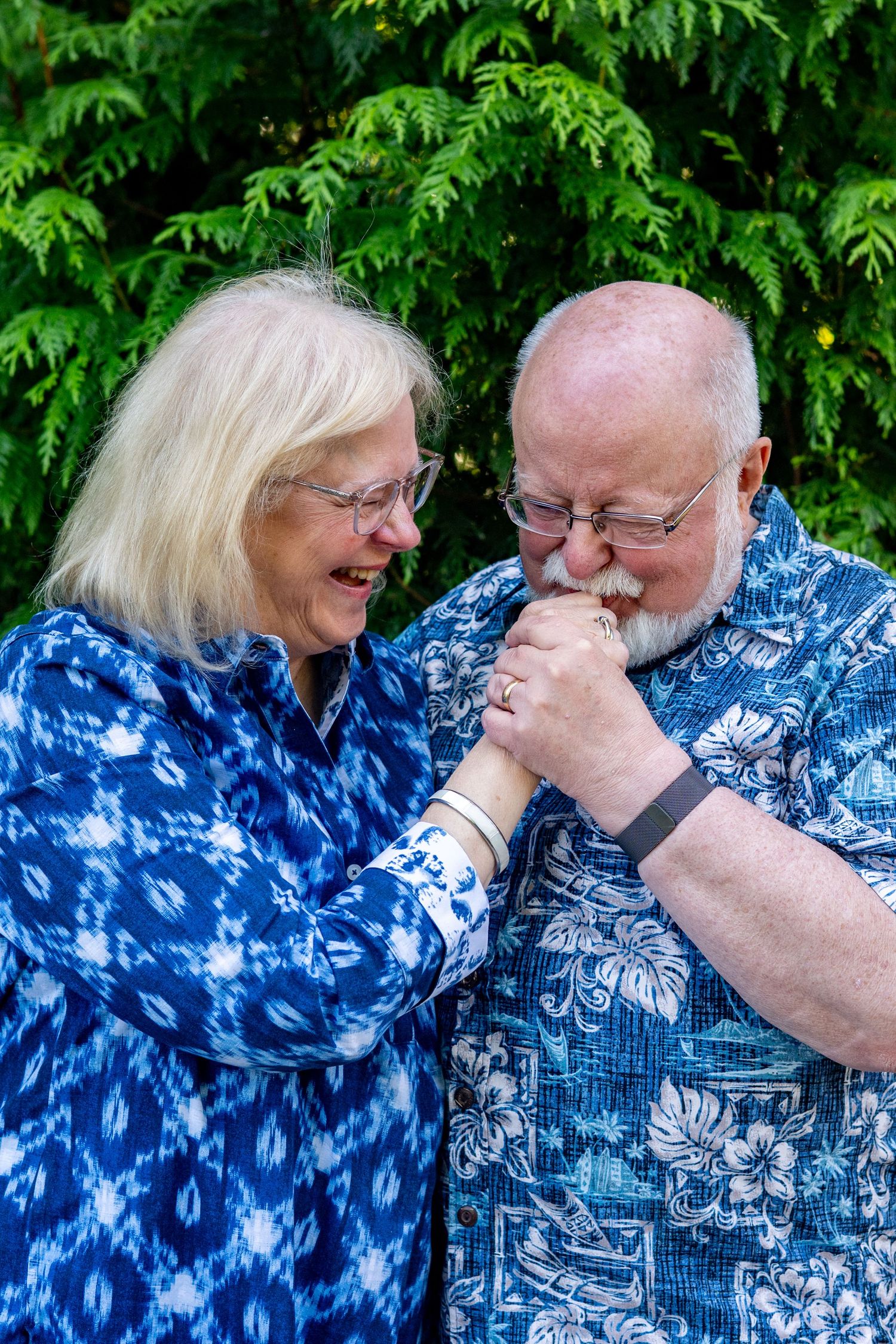 A couple wearing matching blue Hawaiian shirts share a tender romantic moment in a garden setting.