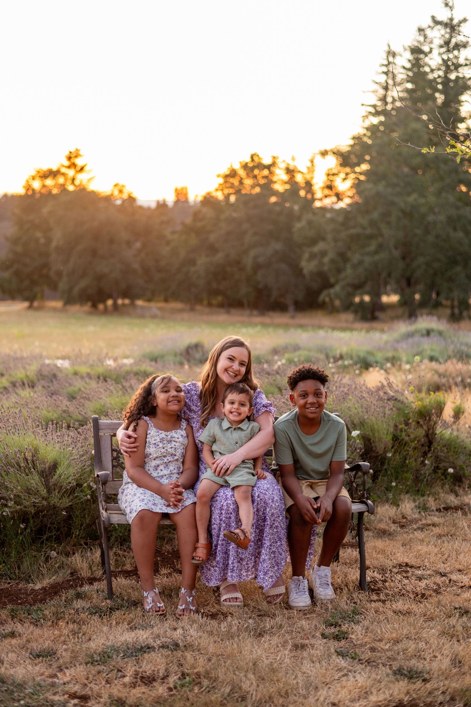 A joyful group sits together on a rustic wooden bench in a sunlit field during golden hour.