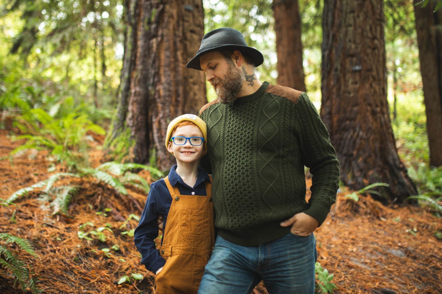 A couple in cozy autumn attire enjoys a romantic stroll through a sunlit redwood forest.