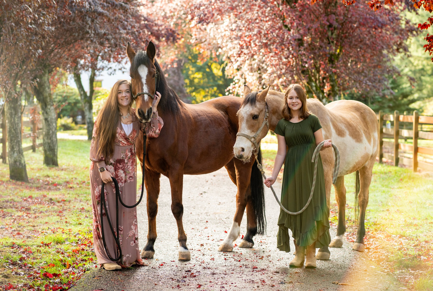 Group poses with two horses on tree-lined autumn path with falling leaves.