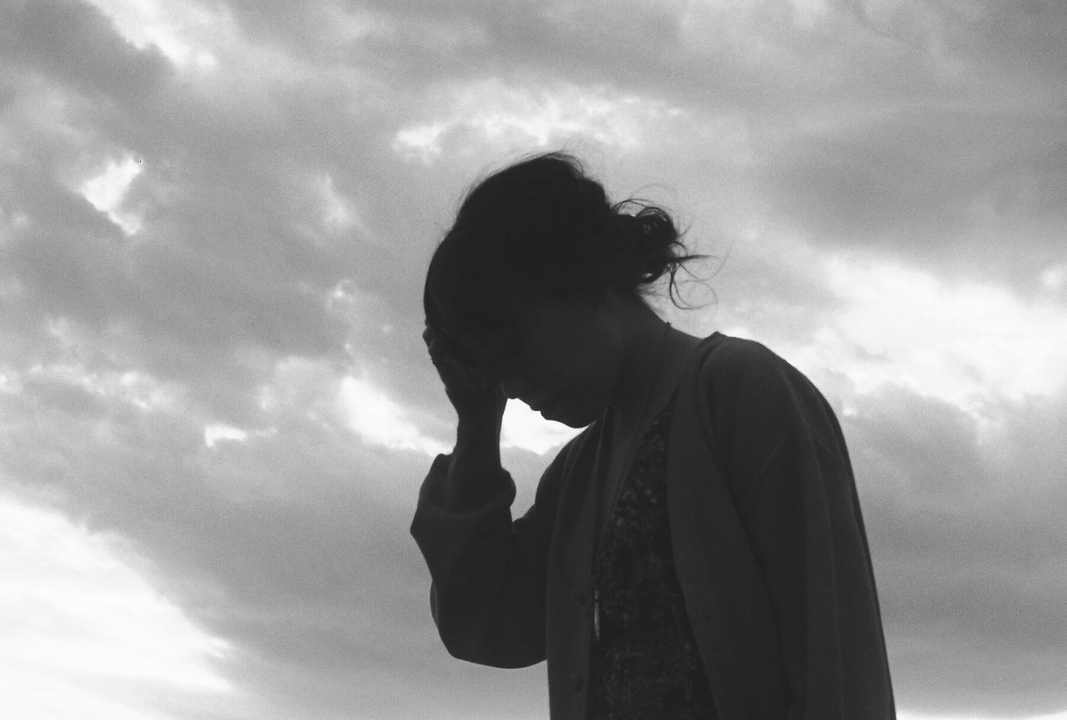 Silhouette figures in profile against a dramatic cloudy sky create a moody black and white composition.