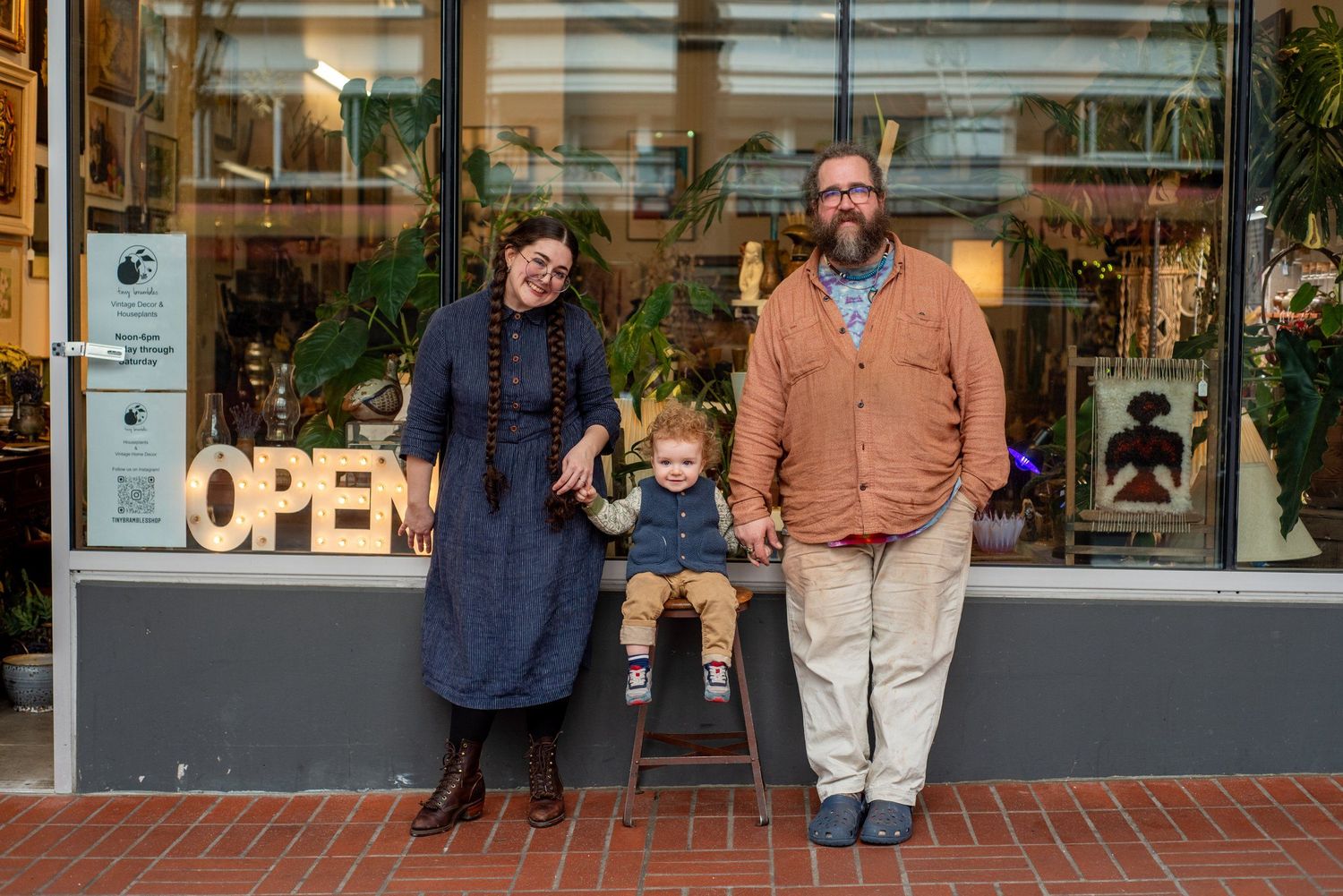A small group stands outside a storefront with an OPEN sign in the window.