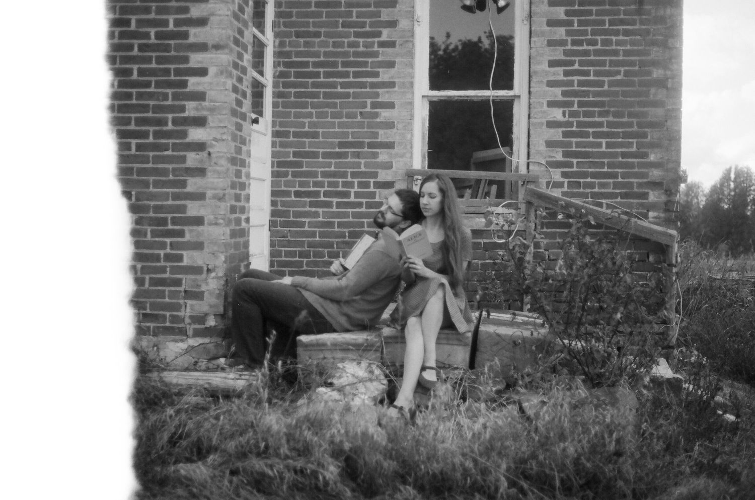 Black and white photo of two figures gardening near a brick house with plants along the facade.