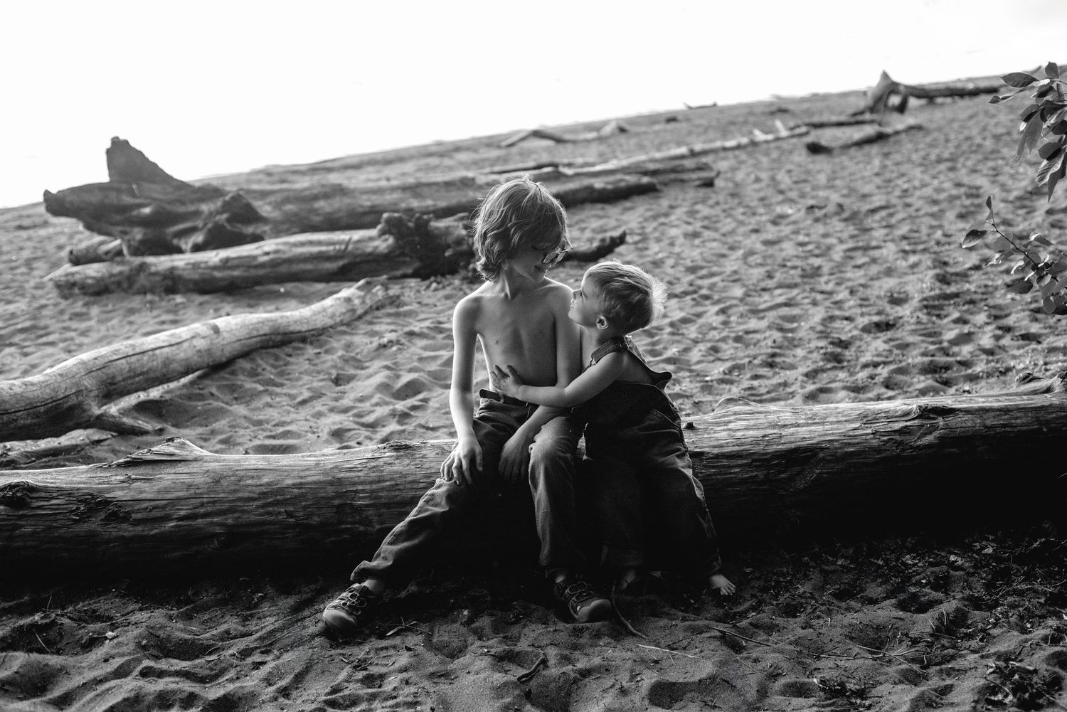 A vintage black and white photo of children sitting on driftwood at the beach.