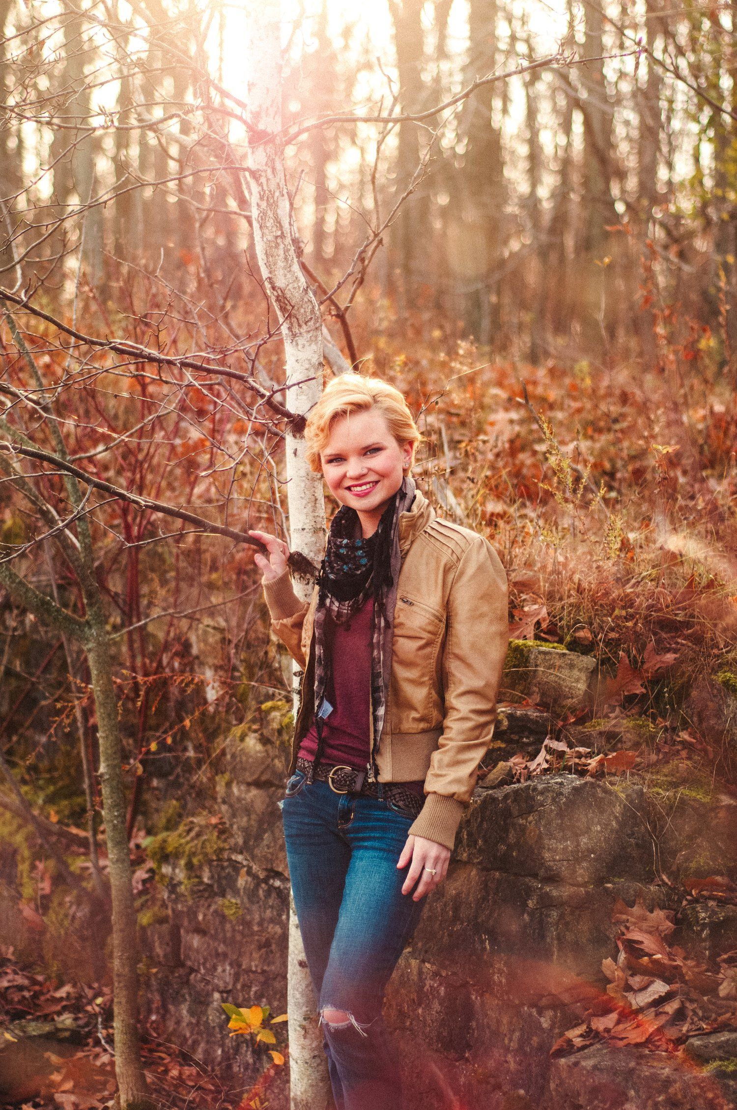 An autumn portrait in a forest with golden sunlight filtering through bare branches.