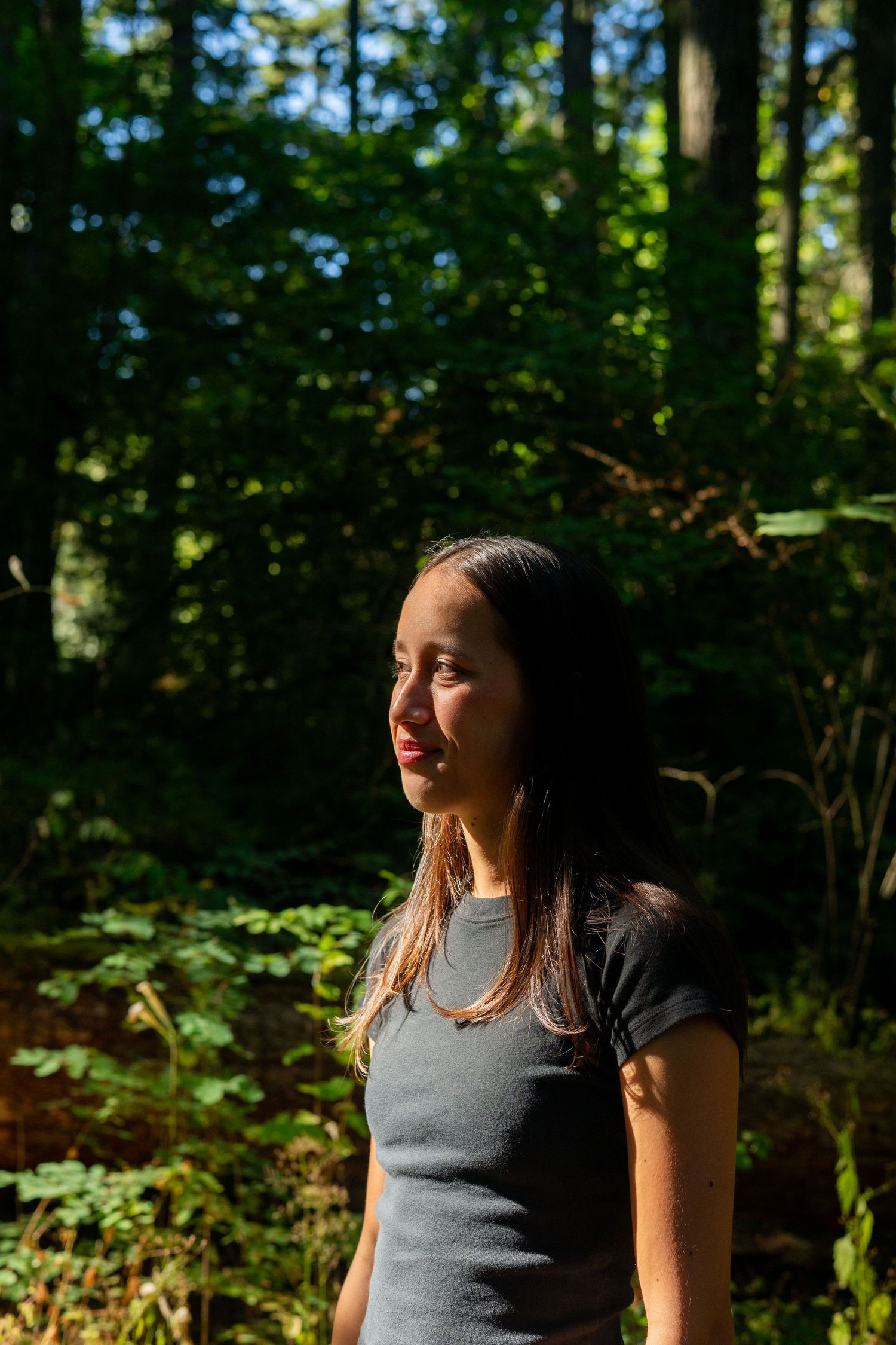 Sunlit portrait in a forest with greenery and dappled lighting creating a natural outdoor atmosphere.