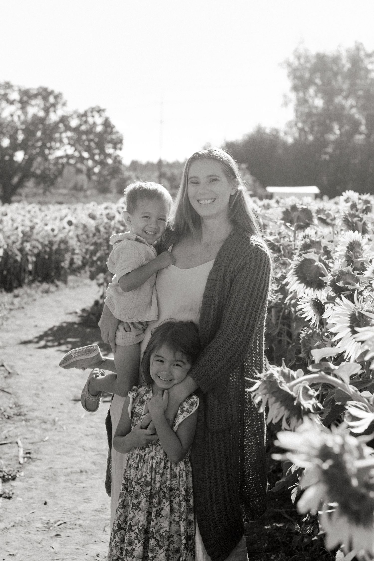 A group poses together in a sunlit sunflower field during a bright summer day.