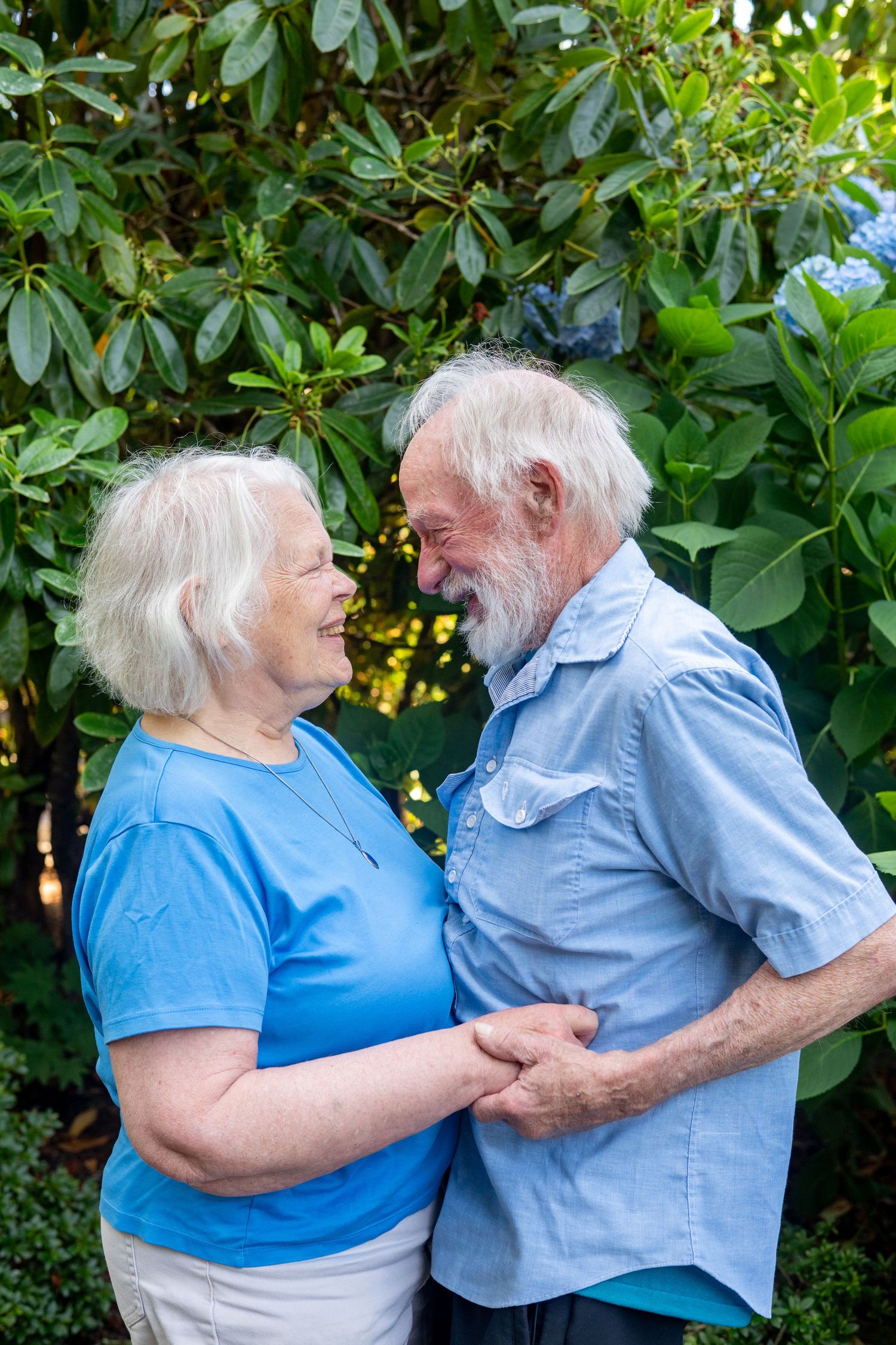 Happy elderly couple dancing together outside in a garden setting while wearing coordinating blue outfits.