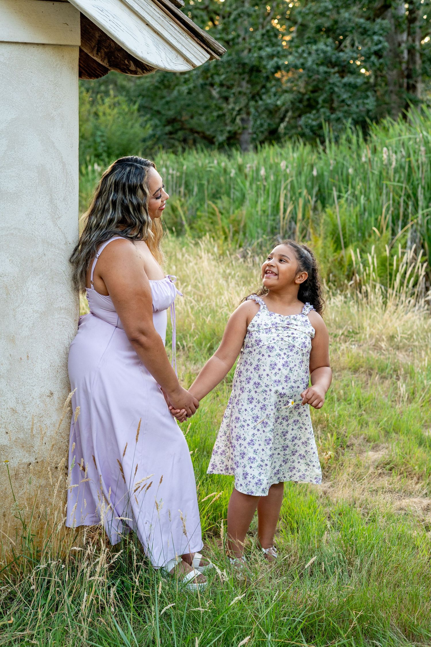 A parent and child share a joyful moment together in a sundress and floral dress against a natural outdoor backdrop.