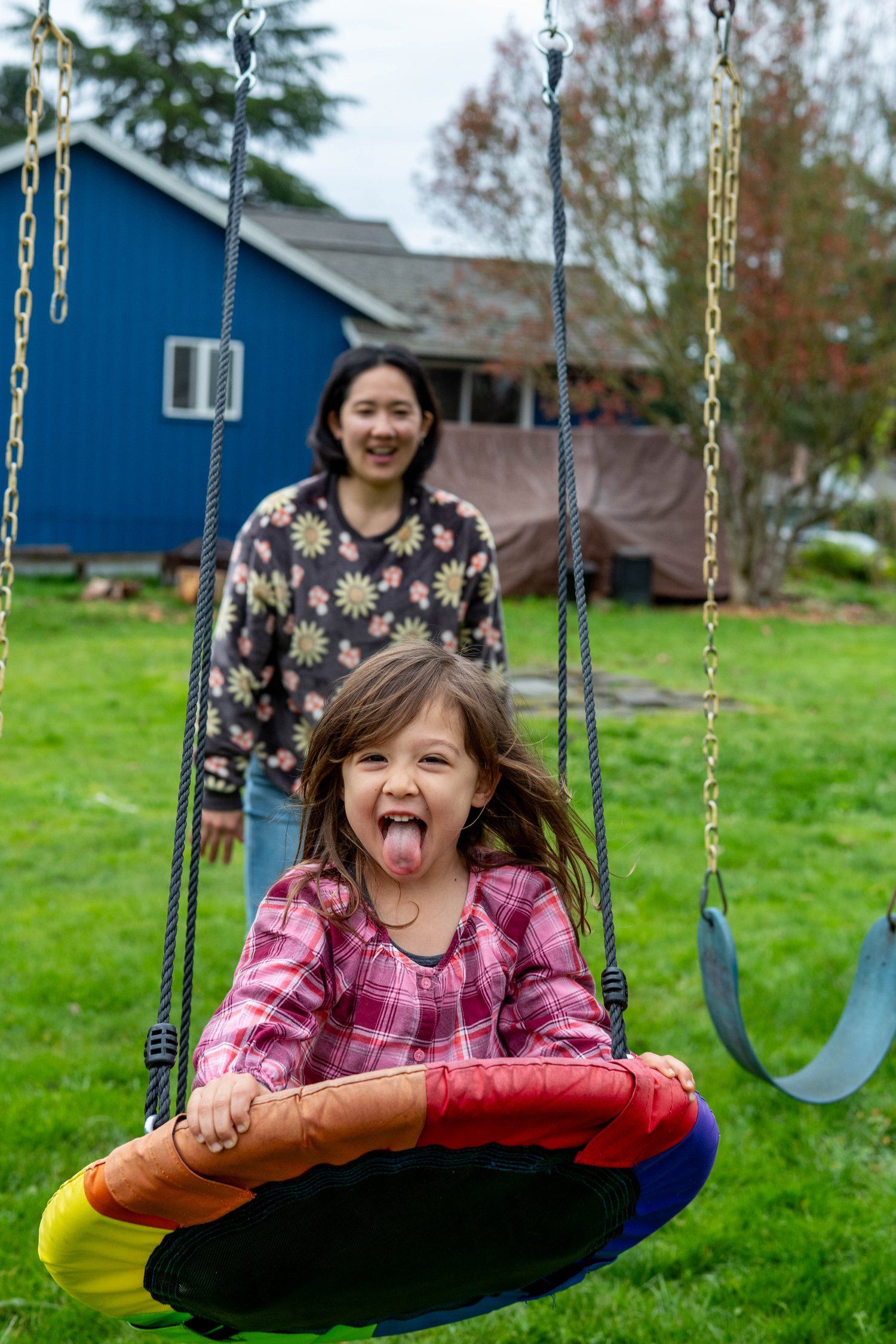 Joyful child laughing while swinging on playground with blue building in background.