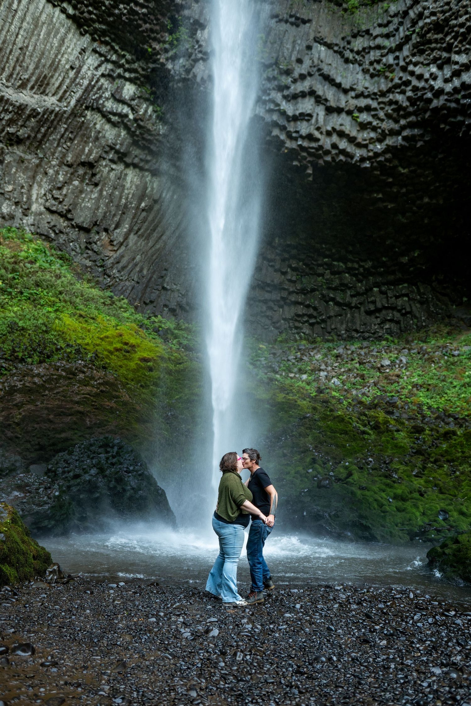 A couple shares an intimate moment beneath the majestic Latourell Falls waterfall in Portland, Oregon.