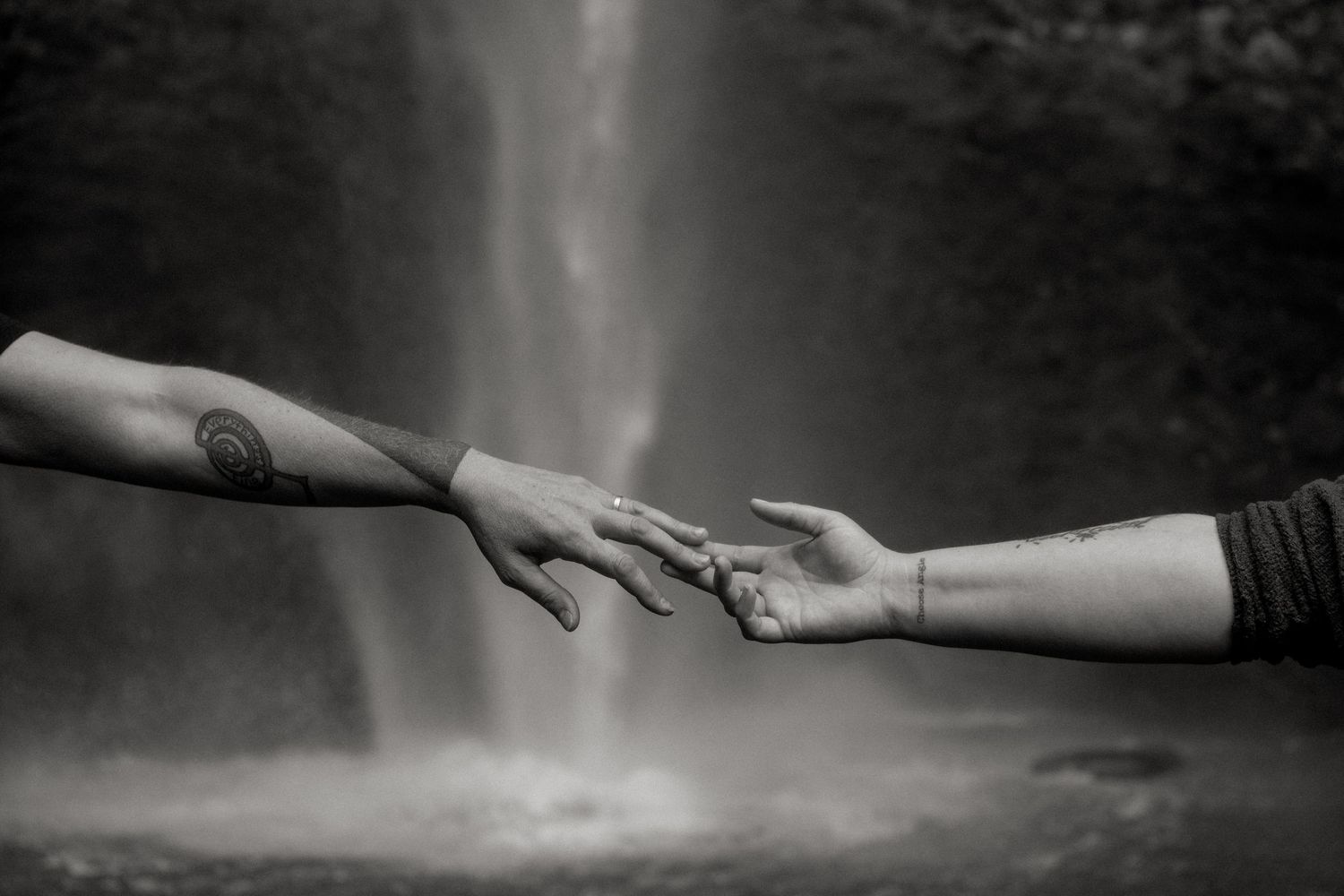 Two ethereal hands reaching for each other across a dark void in a dramatic black and white photograph.