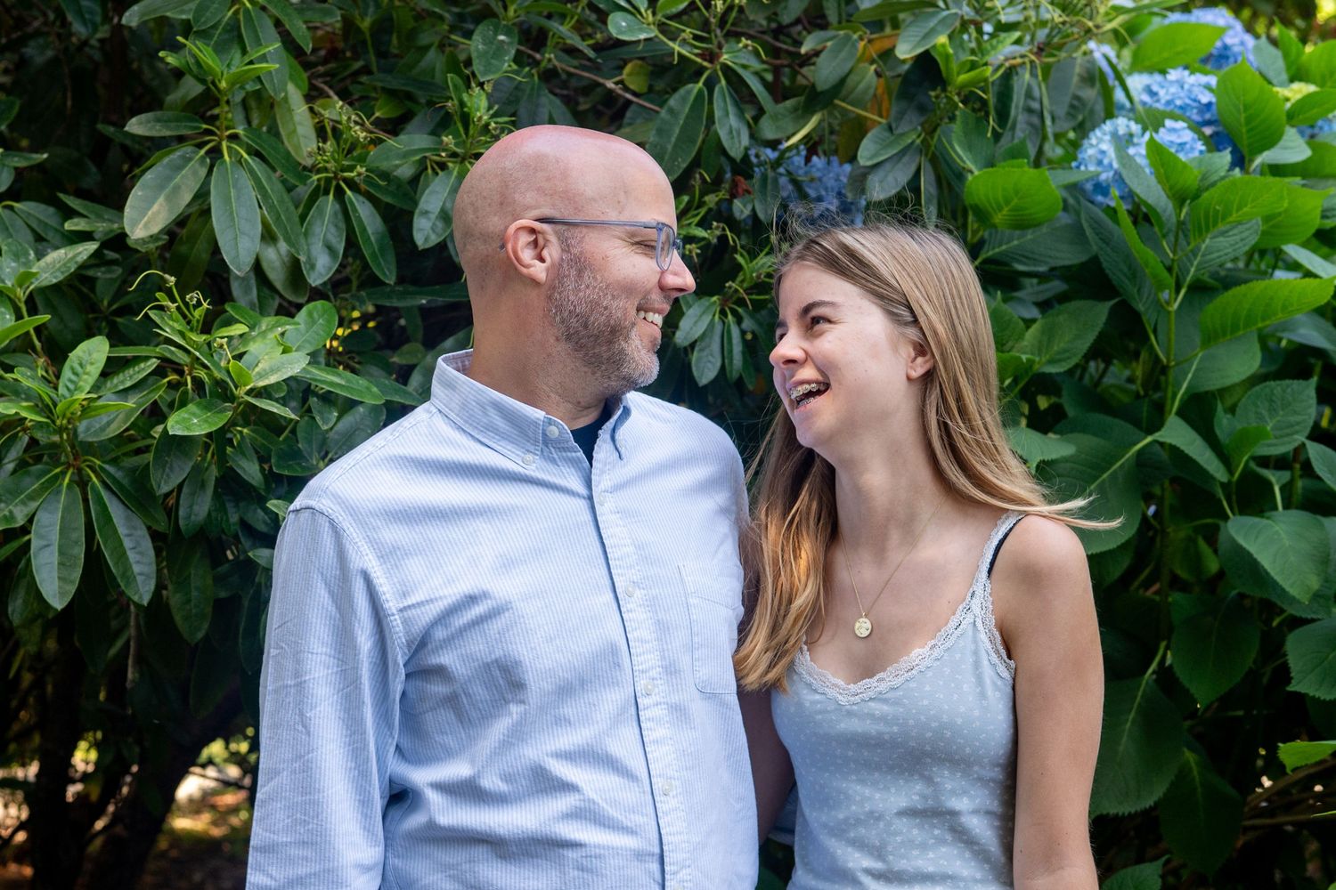 Couple photographed through foliage sharing loving moments in a garden setting during outdoor photo session.