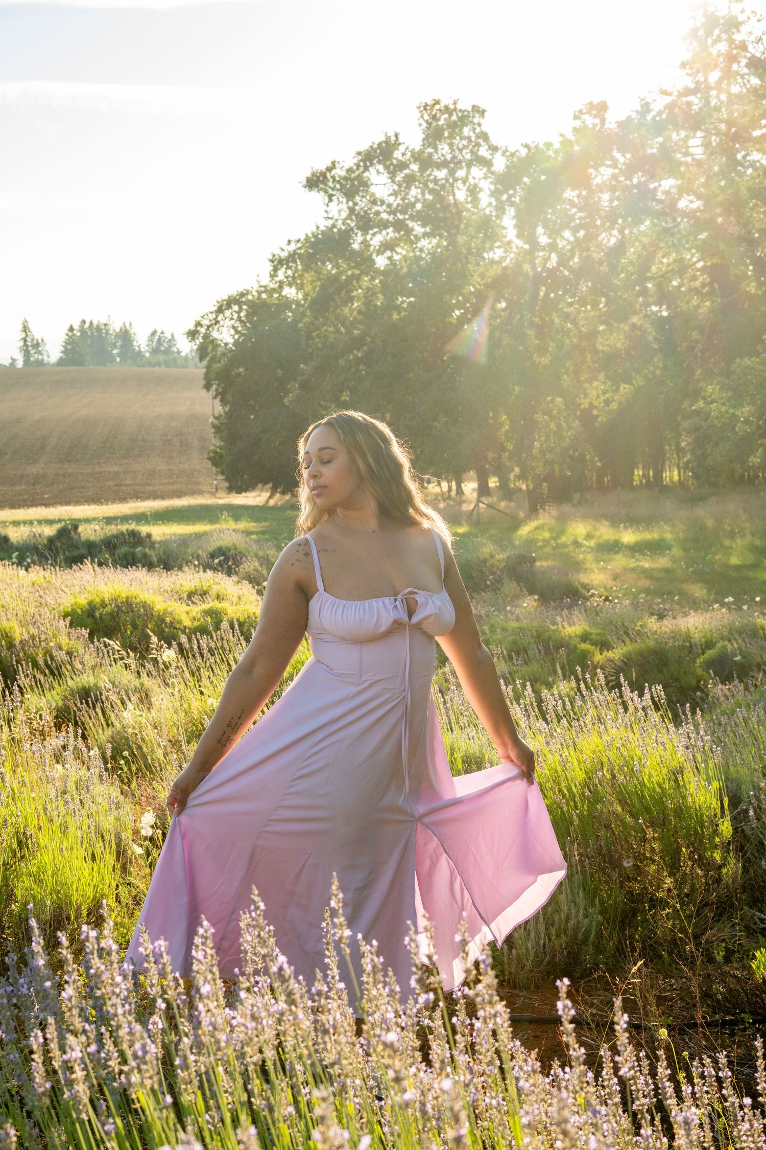 Backlit figure in white dress dances through a colorful lavender field at sunset creating a dreamy summer scene.