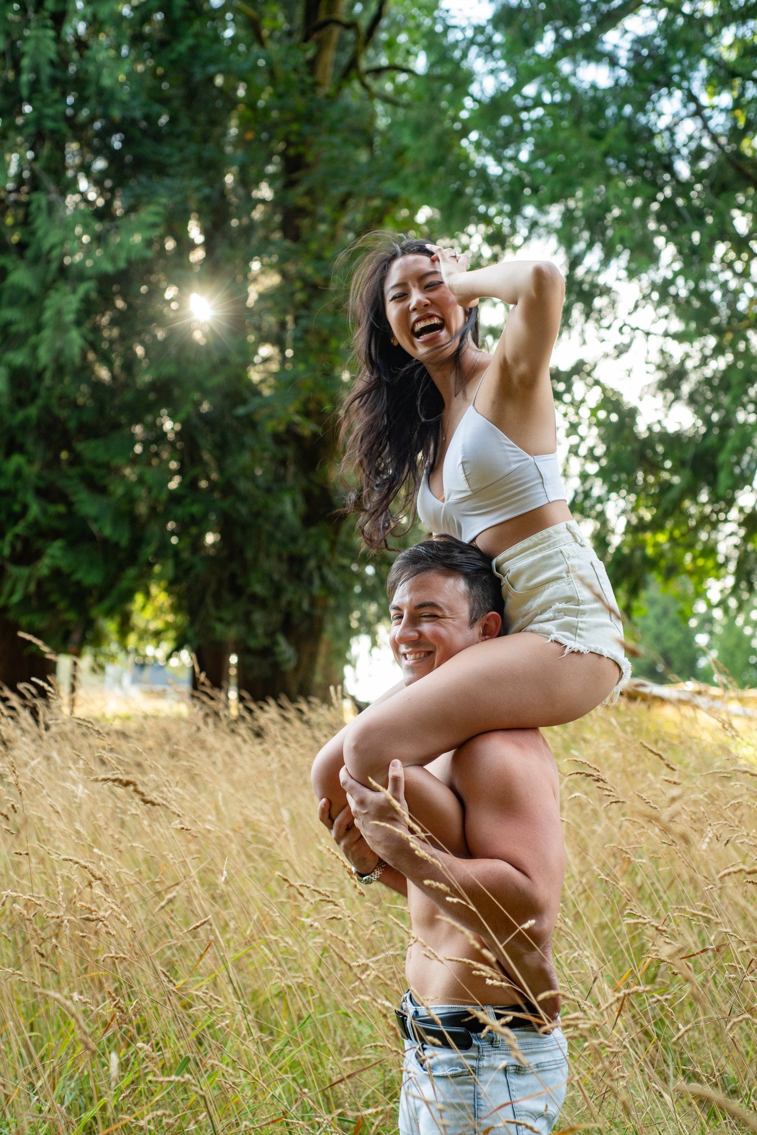 A playfull moment shared between two people in tall grass during sunset with trees in the background.
