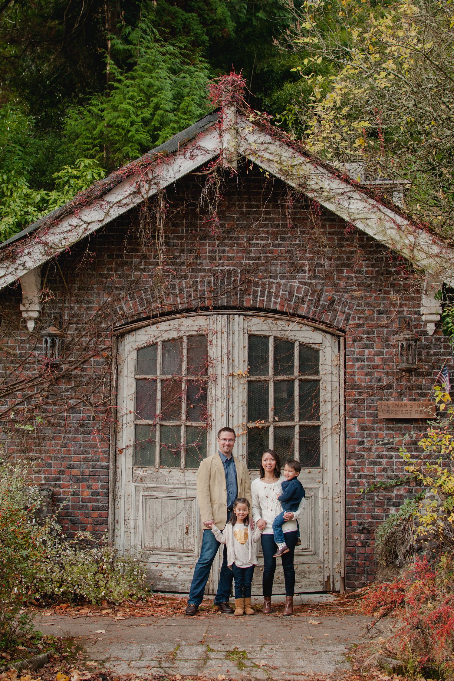 A rustic brick building with arched windows and overgrown vines creates a charming backdrop for a family portrait.