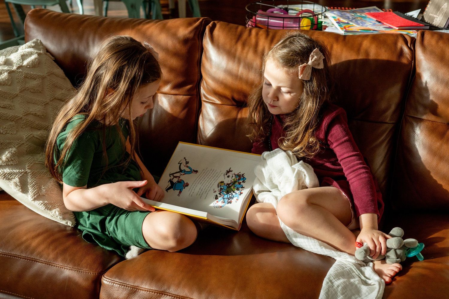 Two readers sharing a book together on a brown leather couch.