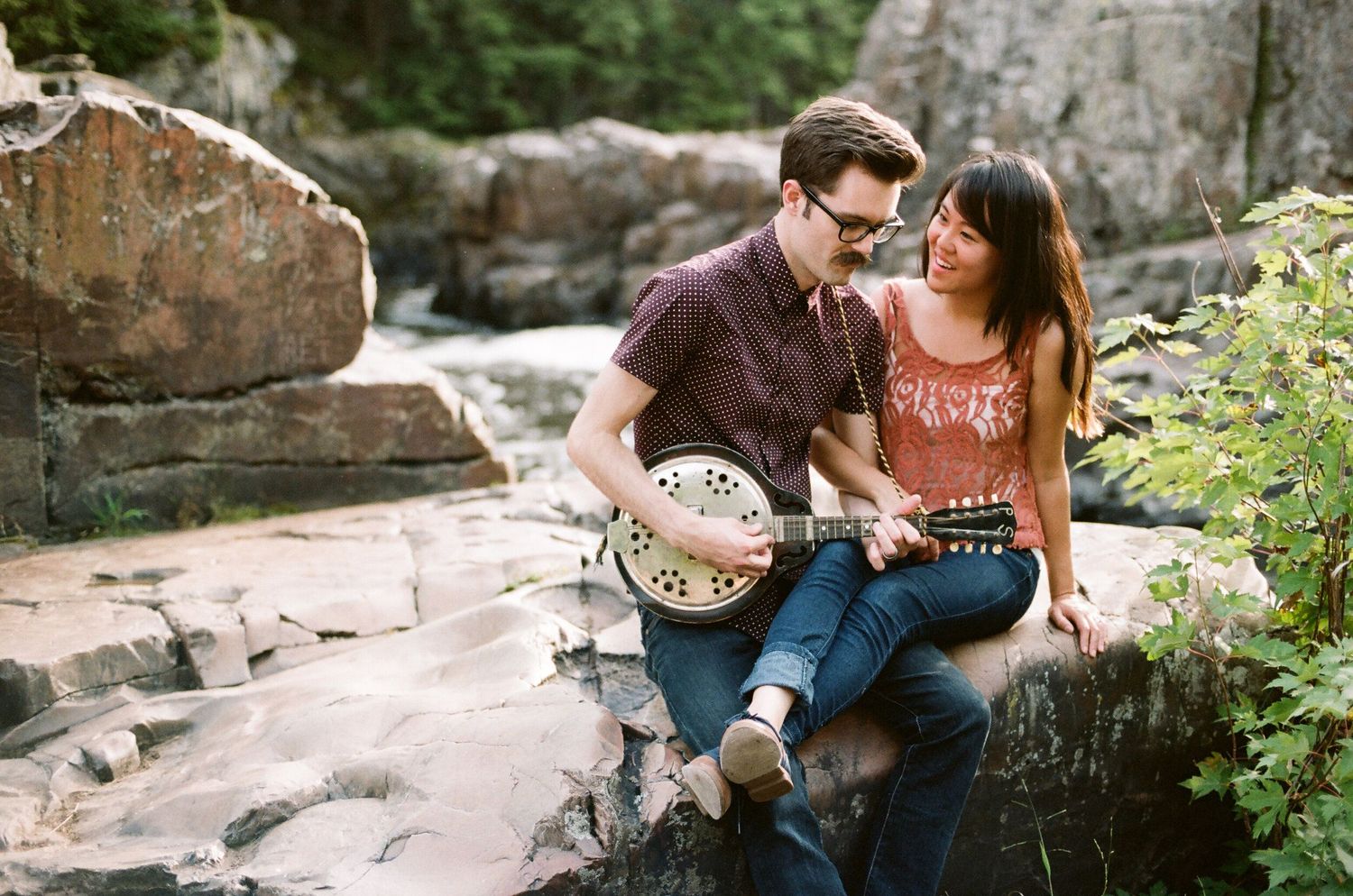 A couple sits together on rocky terrain during an intimate outdoor photoshoot.