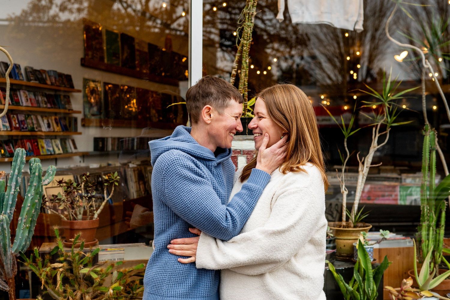 Joyful couple embracing and laughing together outside a garden shop with string lights.