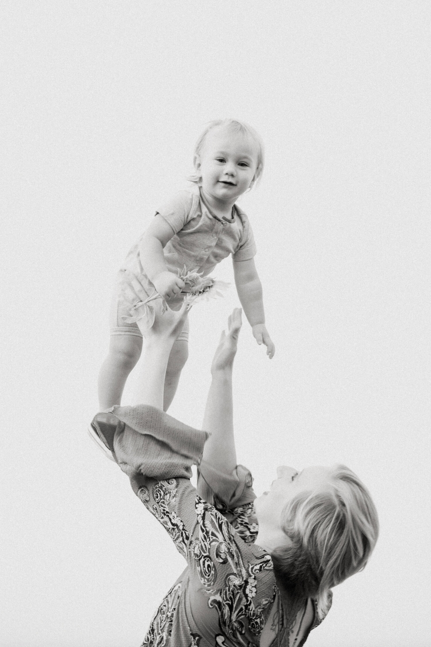Black and white portrait capturing a playful moment between parent and child against white background.